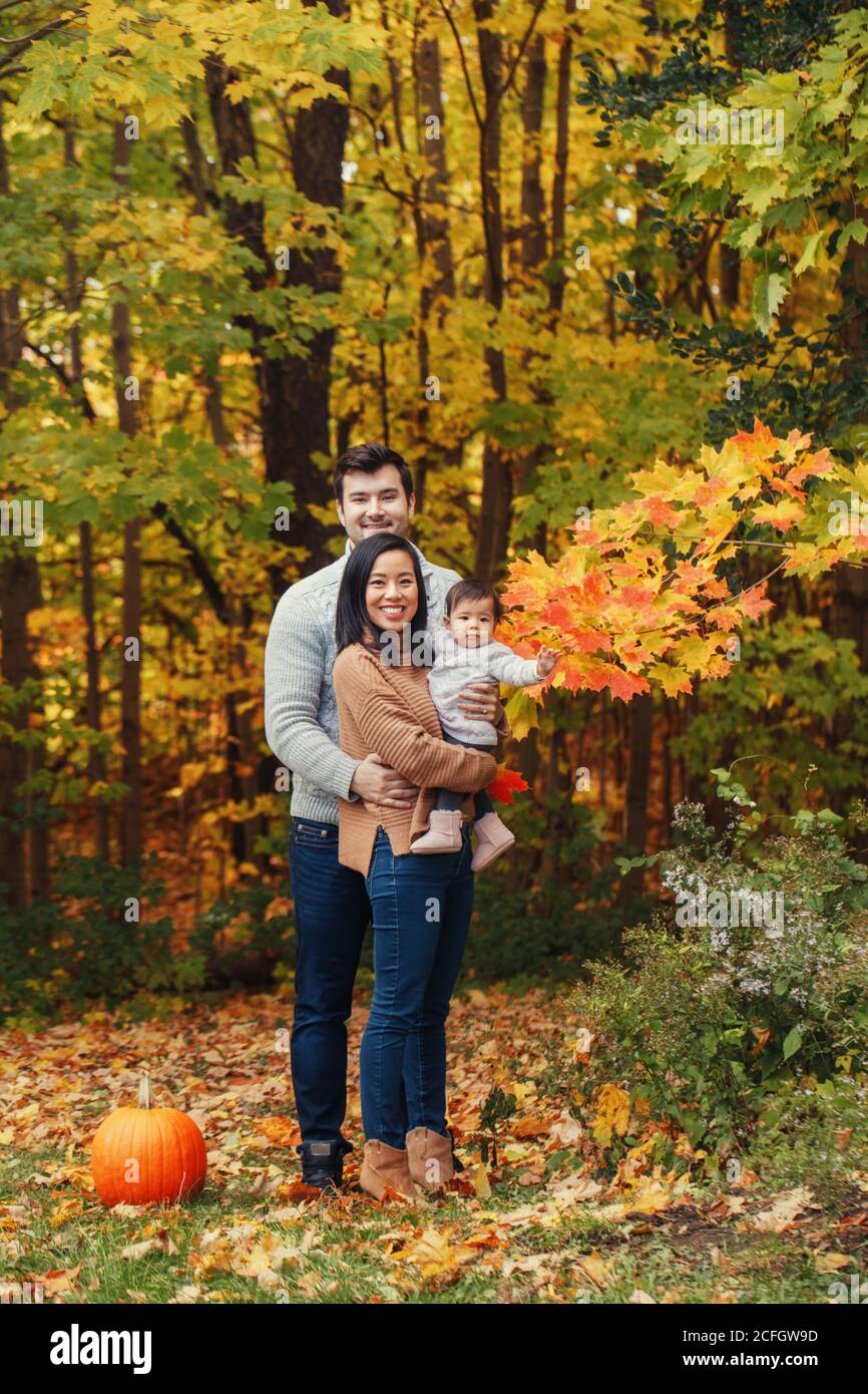 Asiatische chinesische Mutter und kaukasischen Vater Papa mit Baby Mädchen im Herbst Park im Freien. Familienspaziergang posiert im Herbstwald mit rotem Kürbis. Halloween Stockfoto