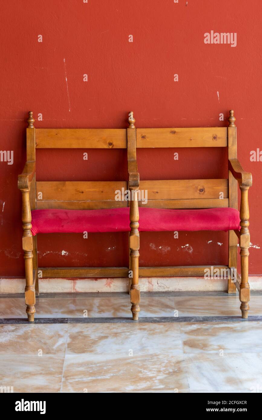 Ein antiker hölzerner Doppelsitz oder Stuhl mit roten Kissen aus Holz an einer rot bemalten Wand. Stockfoto