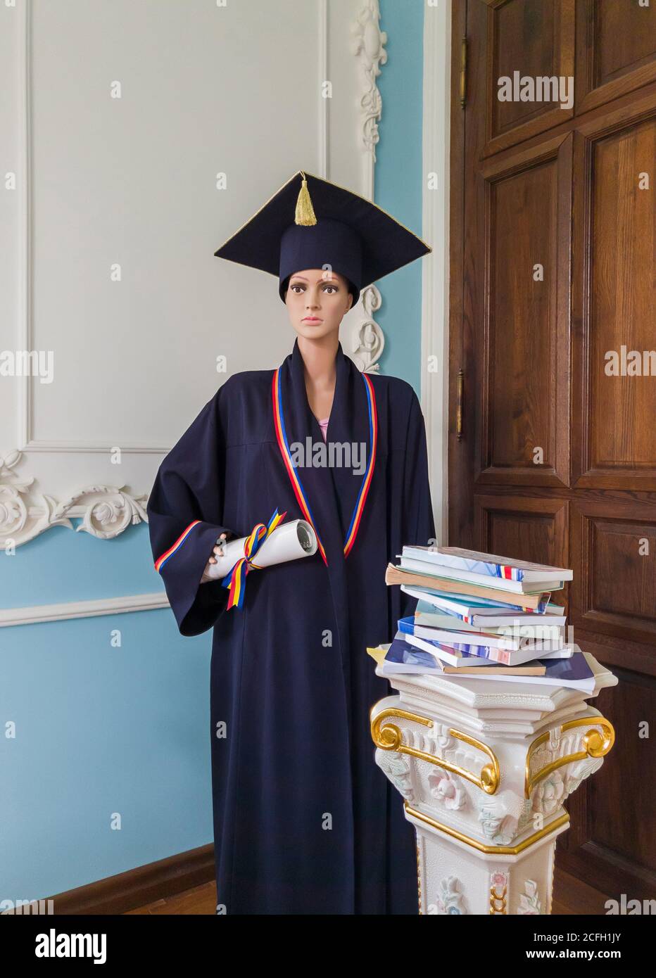 Student Schaufensterpuppe, in einer Bibliothek, gekleidet als Absolvent mit einer schwarzen akademischen Kappe und Kleid, hält ein Diplom in der Hand. Wunderschön verzierte alte Pil Stockfoto