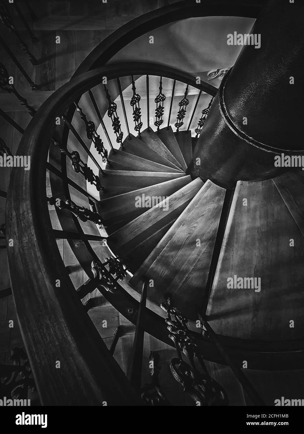 Ein Blick auf eine alte Wendeltreppe. Hölzerne Rundtreppe mit verzierten Metallgeländer, schwarz-weiß vertikale Aufnahme, Innenarchitektur de Stockfoto