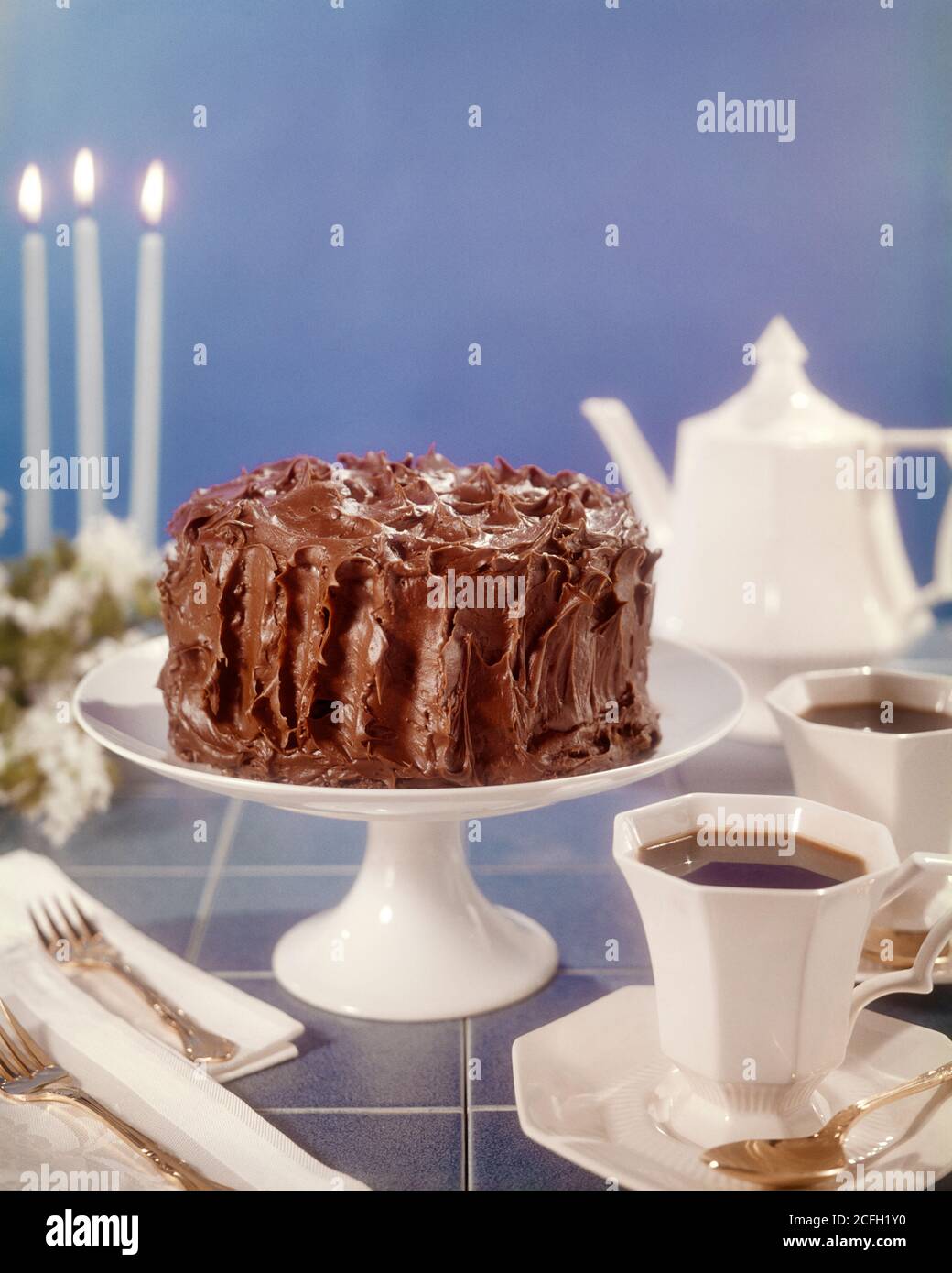 70ER JAHRE SCHOKOLADE ICED CAKE AUF WEISSEN KUCHEN STAND KAFFEEKANNE TASSEN  UND UNTERTASSEN GABELN SERVIETTEN DREI BLAUE KERZEN - KF8548 PHT001 HARS  TISCHPLATTE Stockfotografie - Alamy