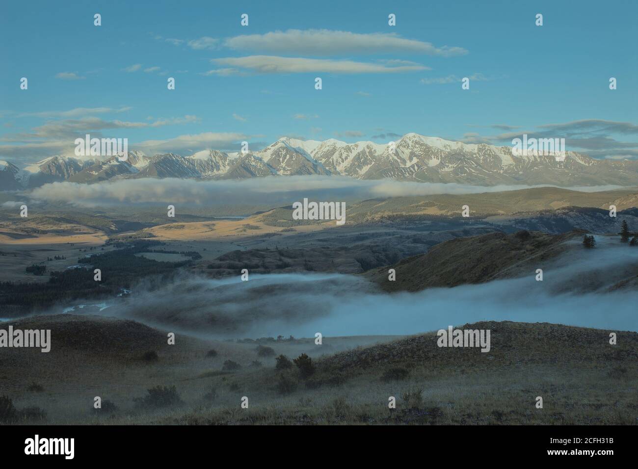 Morgenlandschaft mit einem Flusstal, niedrigen Wolken schleichend auf dem Boden und weißen schneebedeckten Bergen im Hintergrund. Chuya Kamm, Altai Berge, Sibirien, Russland .. Stockfoto