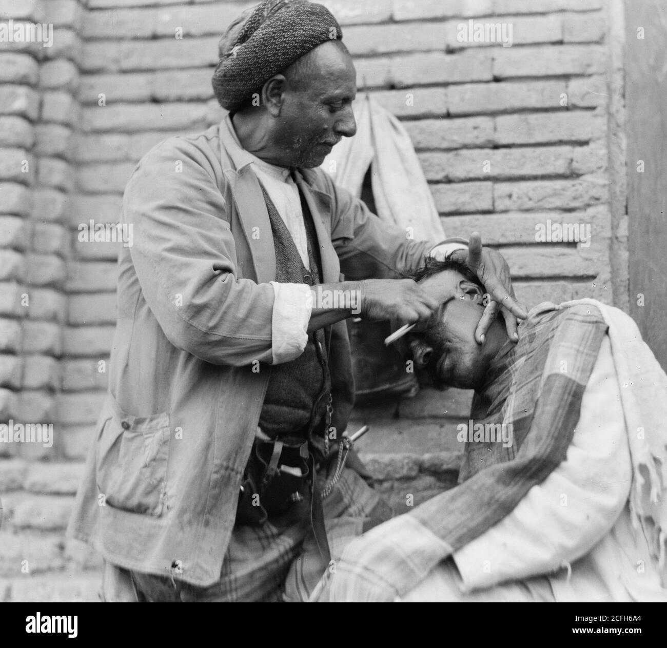 Originalunterschrift: Irak. (Mesopotamien). Bagdad. Ansicht von Straßenszenen und Typen. Straßenbarbier bei der Arbeit - Ort: Irak--Bagdad ca. 1932 Stockfoto