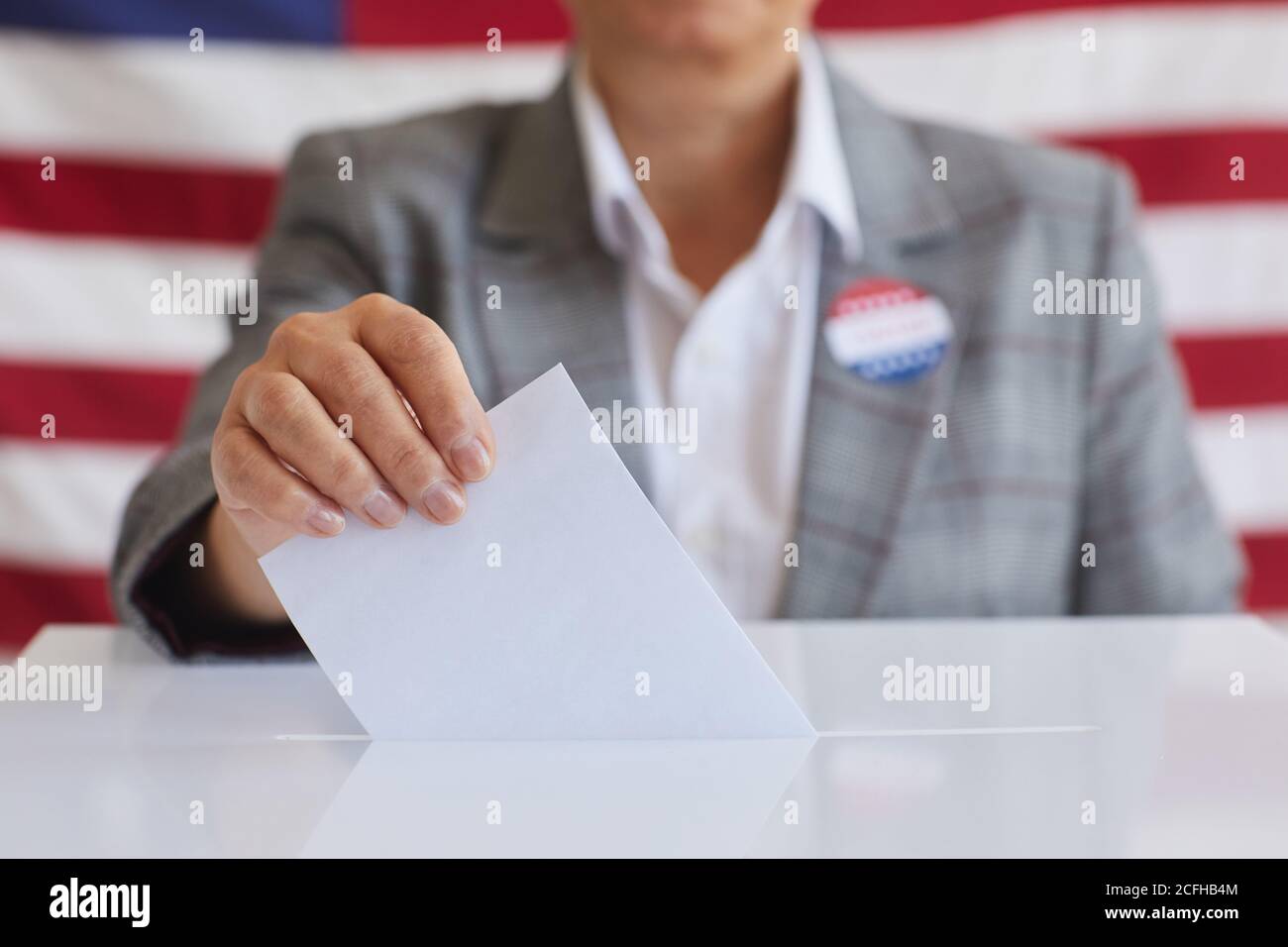Nahaufnahme einer reifen Frau, die am Wahltag gegen die amerikanische Flagge steht und Stimmzettel in die Wahlurne legt, Platz kopieren Stockfoto