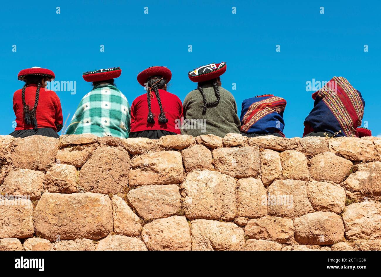 Peruanische indigene Quechua Menschen sitzen auf einer Inka-Mauer, Chinchero, Provinz Cusco, Peru. Stockfoto