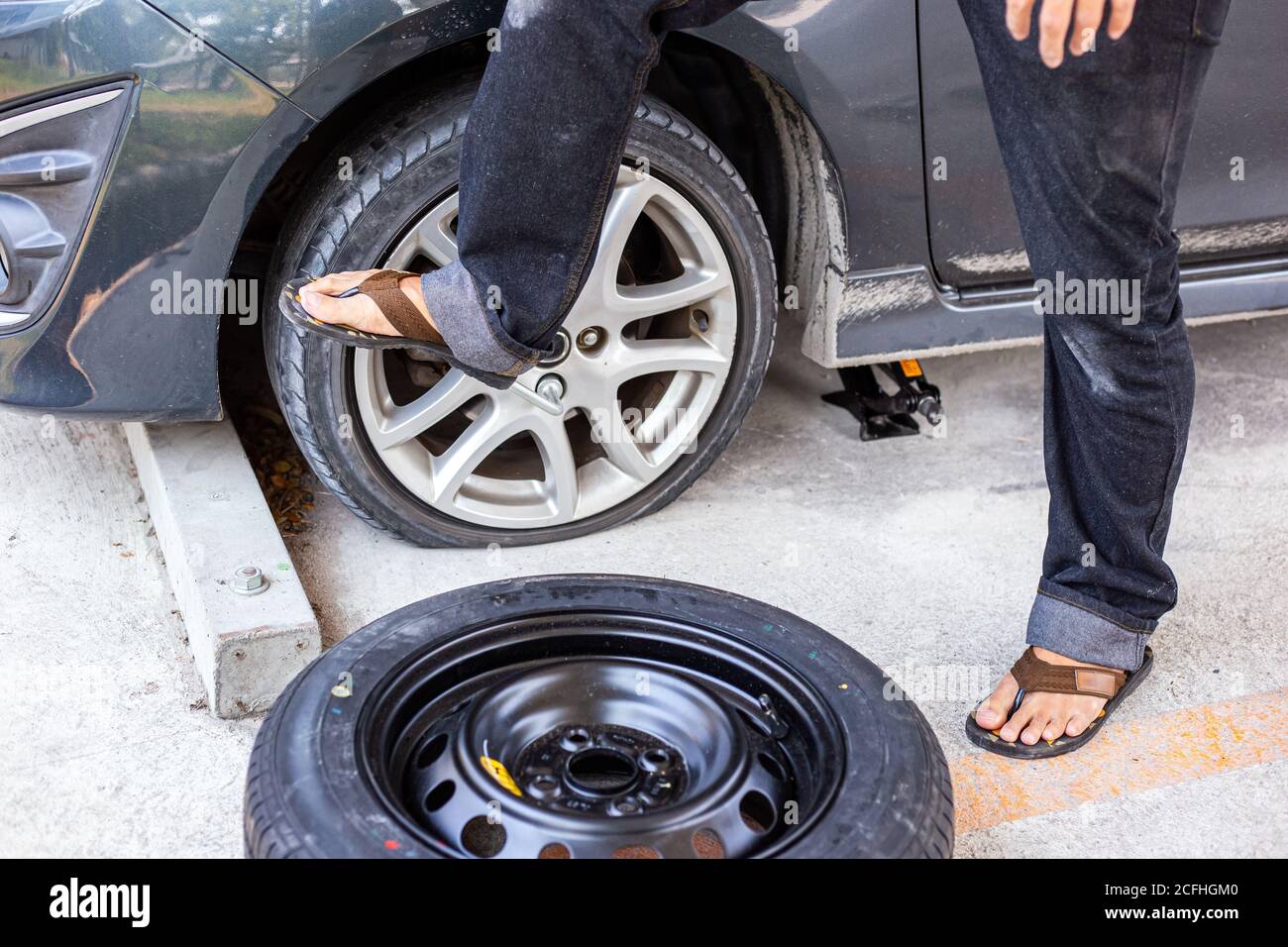 Wechseln Sie einen flachen Autoreifen auf dem Parkplatz mit Reifenpflege, beschädigte Autoreifen Stockfoto