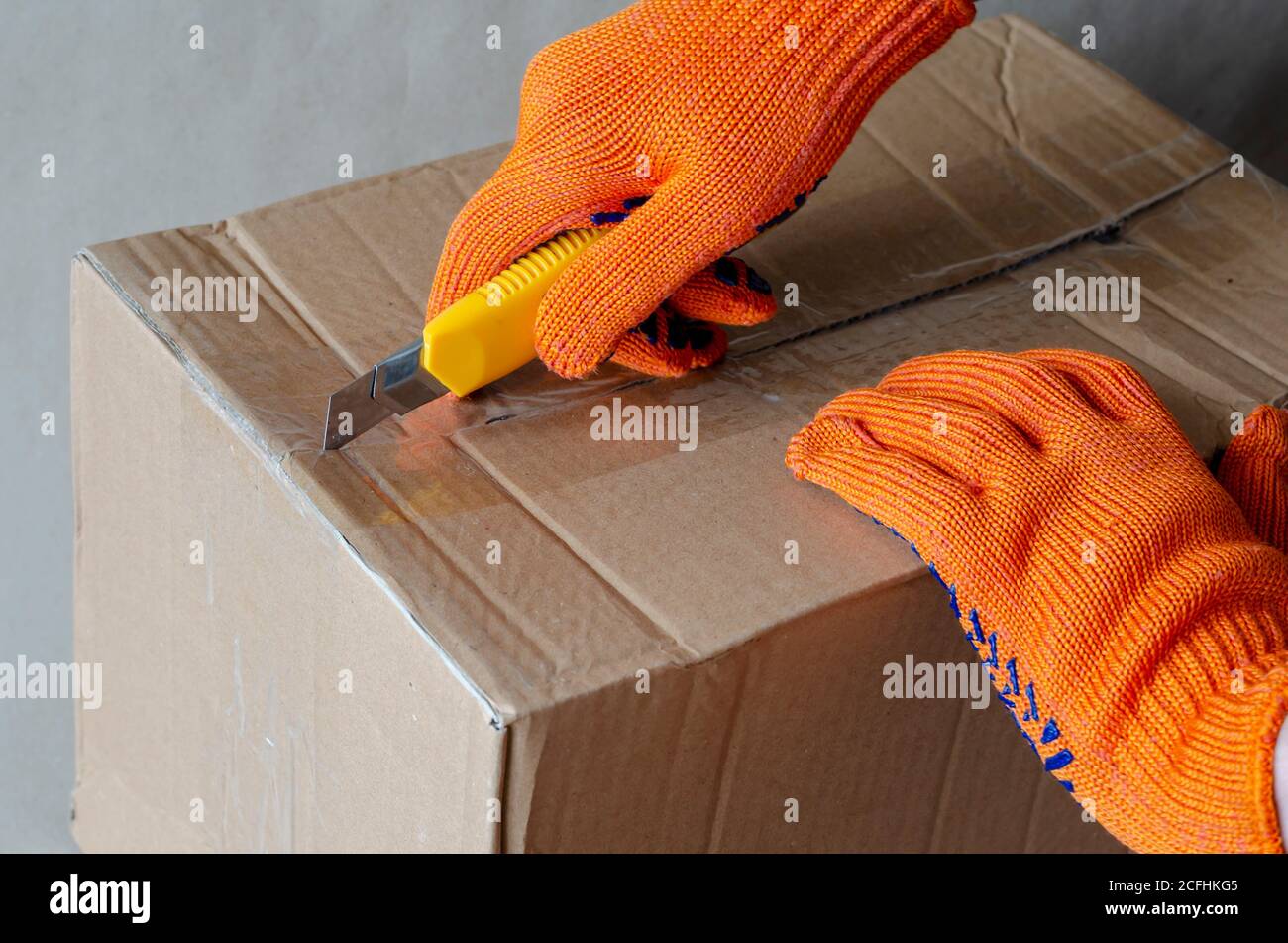 Ein Arbeiter, der Schutzhandschuhe trägt, öffnet einen Karton. Eine Hand mit einem Messer schneidet das Klebeband auf der Verpackung. Logistik und Lieferservice. S Stockfoto