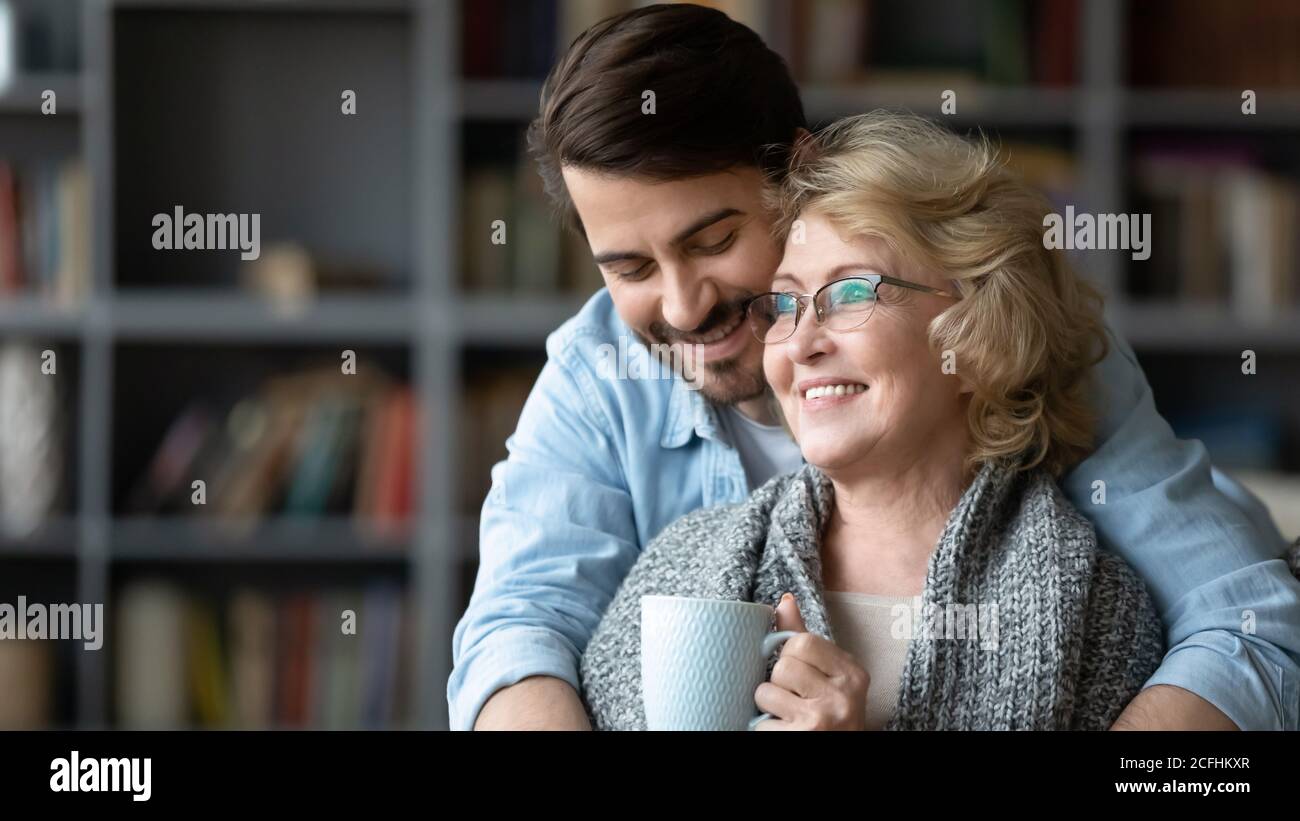 Lächelnder junger Mann umarmt reife Mutter trinkt Tee Stockfoto