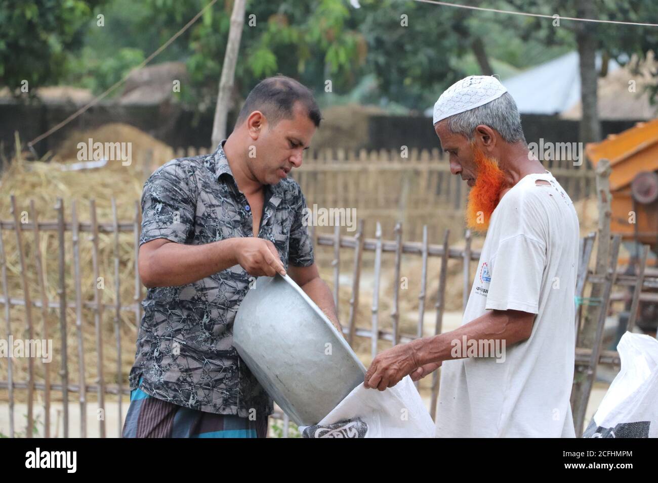 Zwei Bauern füllen einen Sack mit einer Schale geernteter Reiskörner auf einer Farm im ländlichen Bogura, Bangladesch Stockfoto