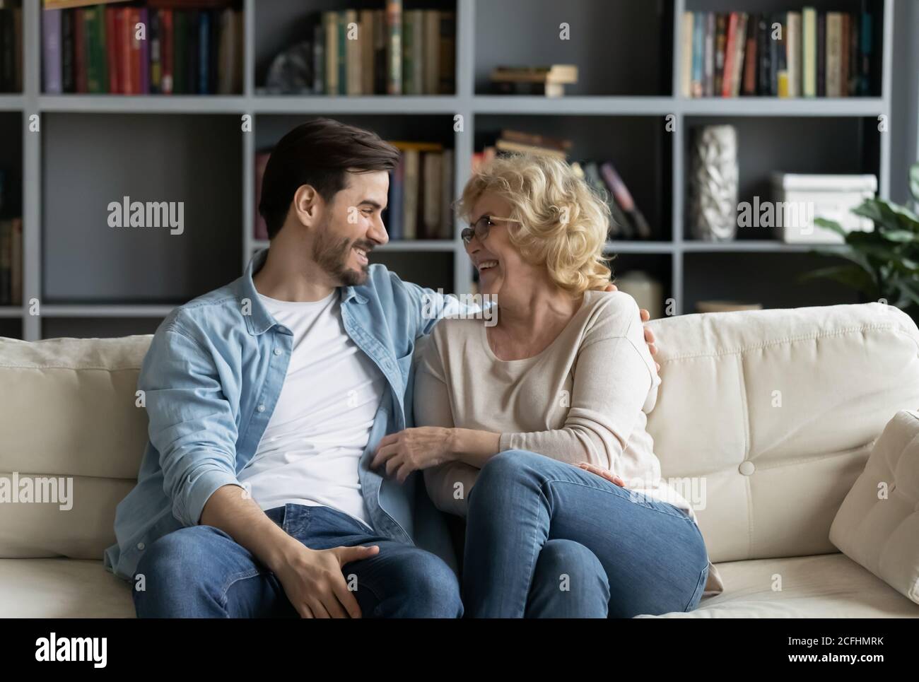 Glückliche reife Frau und junger Mann im Gespräch, auf der Couch sitzen Stockfoto