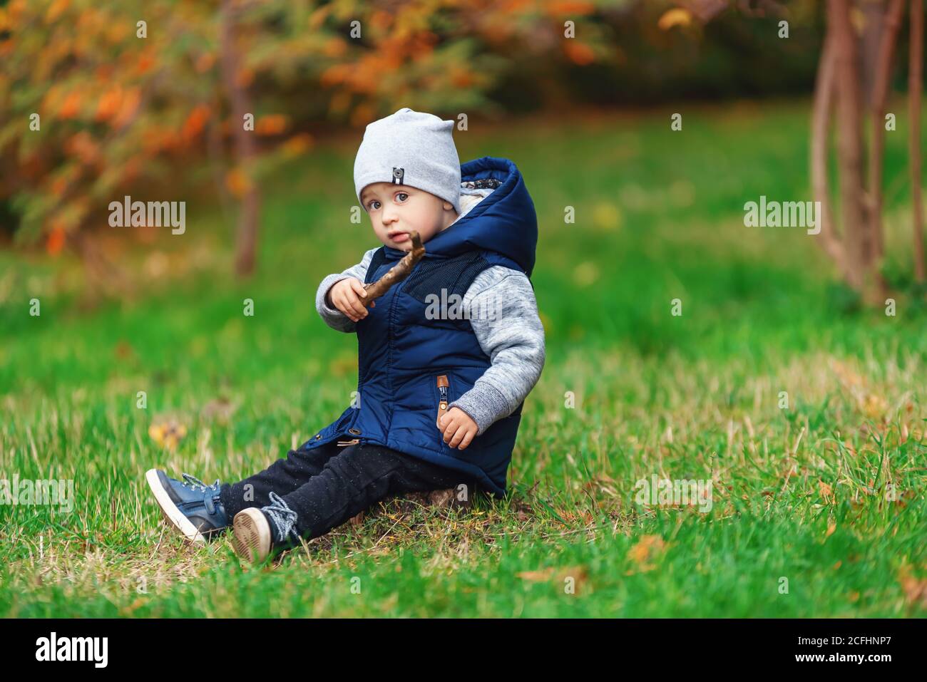 Ein modischer Junge, der im Herbstpark spielt. Kind sitzt auf dem grünen Gras Stockfoto