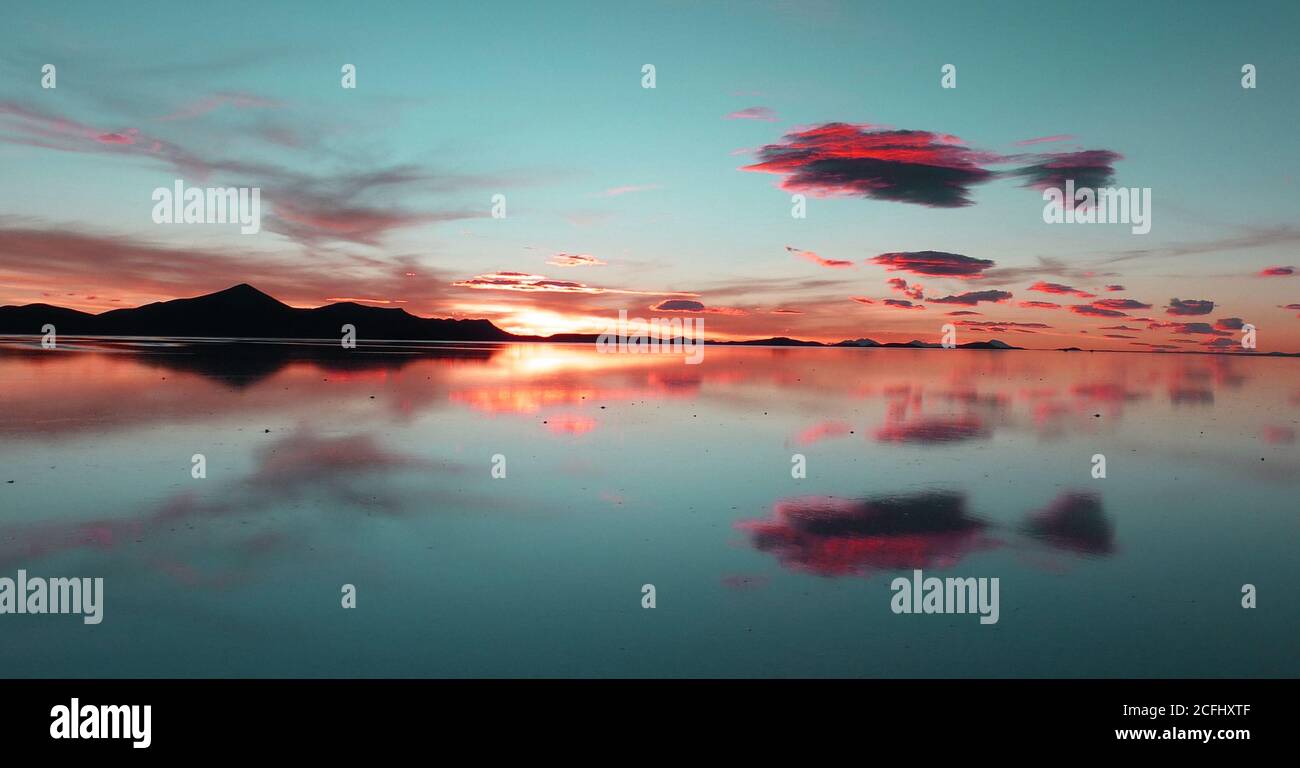 Atemberaubender ungewöhnlicher Sonnenuntergang über dem See Uyuni. Rosa Wolken spiegeln sich im Salzwasser. Wunderschönes Spektakel. Unvergesslicher Anblick. Gelassenheit und Meditation. Stockfoto