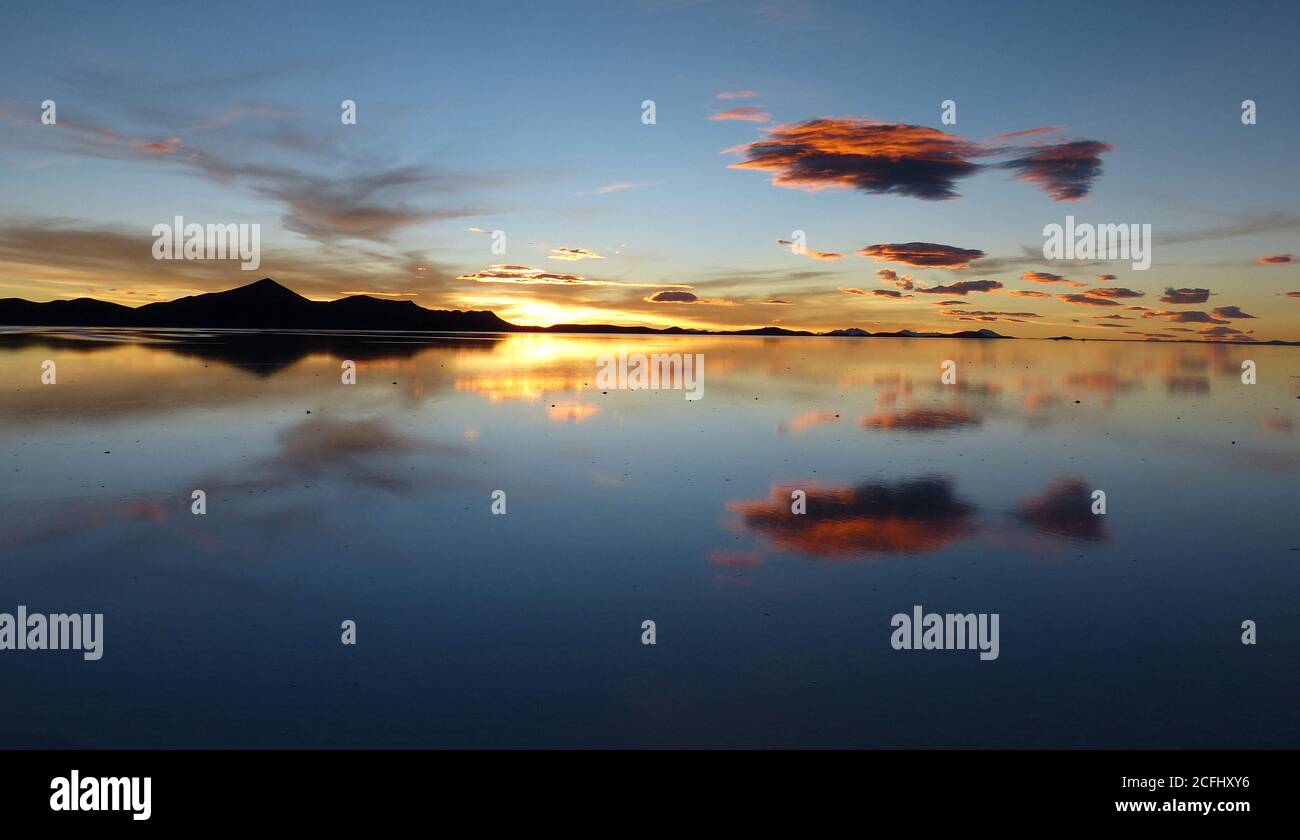 Rosafarbener romantischer Sonnenuntergang über dem Salzsee. Magentafarbene Wolken über dem Salzsumpfgebiet Uyuni in Bolivien. Malerische dunkle Silhouette der Anden Berge. Wunderschöne wilde Stockfoto