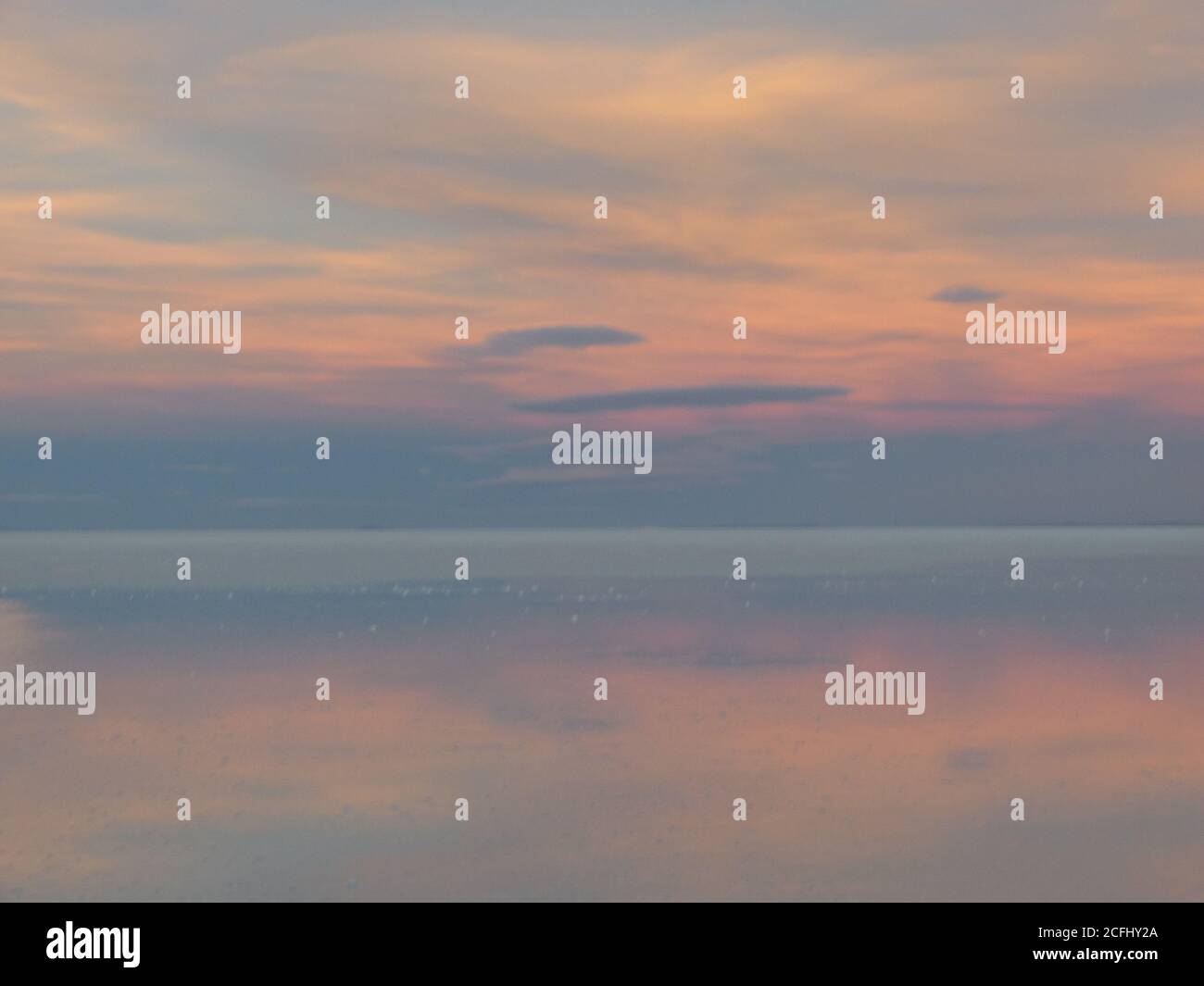 Leicht bewölkt. Sanfter Sonnenaufgang über dem Salzsee. Wolken reflektierten sich auf den Uyuni Salzebenen in Bolivien. Zartfarbener Himmel. Wunderschöne Landschaft am Morgen. Stockfoto