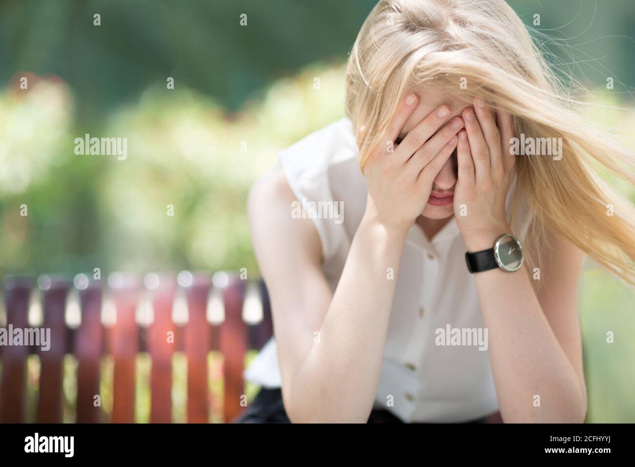 Angst und Depression. Traurige junge Frau in Schmerzen weinend und ihr Gesicht zu bedecken, während sie allein auf einer Parkbank an einem sonnigen Tag sitzt. Stockfoto