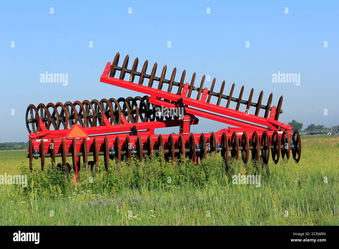 Disc Farm Ausrüstung in einem Bauernhof Feld mit grünen Unkräutern auf dem Land mit blauem Himmel in Kansas . Stockfoto