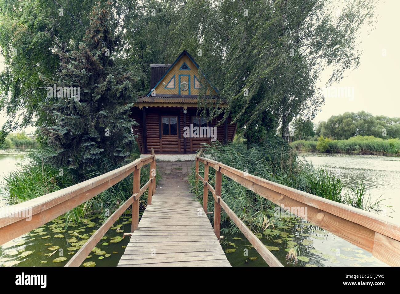 Ukraine, 2. August 2020,Fischerhaus auf der Insel am See im Sommer, grüne Bäume, Holzbrücke, Stockfoto