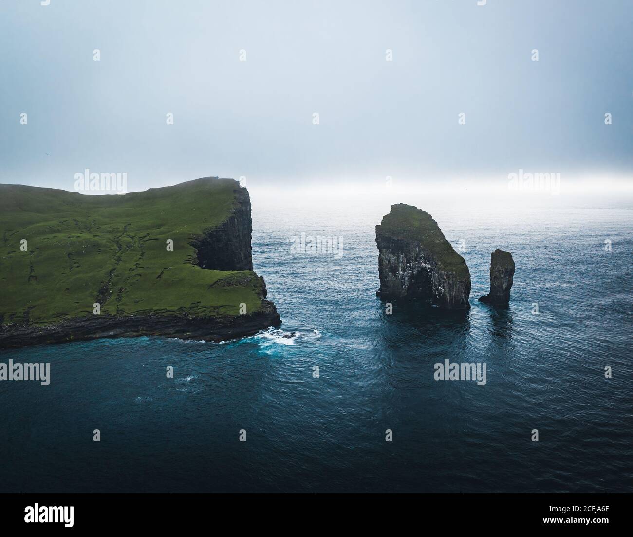 Färöer Inseln Luftdrohnenansicht der Drangarnitr Klippe und Tindholmur Inseln. Aufgenommen während intensiver Wolken im Sommer mit dunkelblauem Wasser des atlantiks Stockfoto