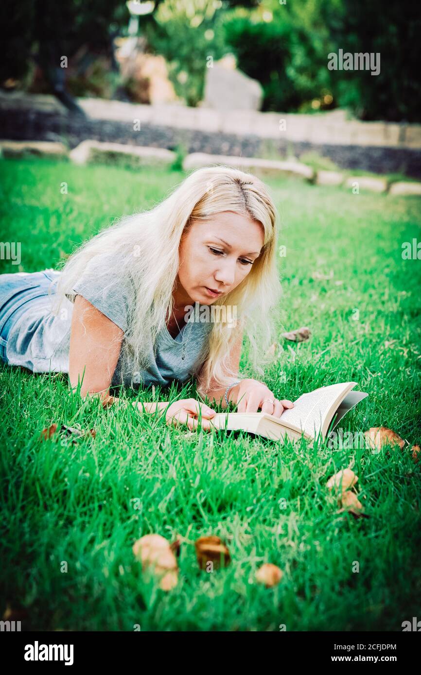 Nahaufnahme einer jungen Frau, die in einem Park ein Buch liest, auf Gras liegend, Foto mit Wirkung Stockfoto