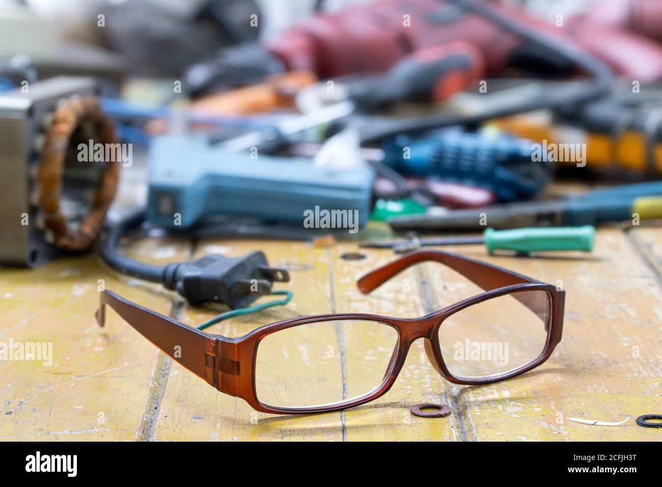 Werkstatt-Desktop von Elektriker-Werkstatt mit seiner Brille. Die Brillen auf einem Tisch voller Werkzeuge und Komponenten für die Reparatur elektrischer Geräte Stockfoto