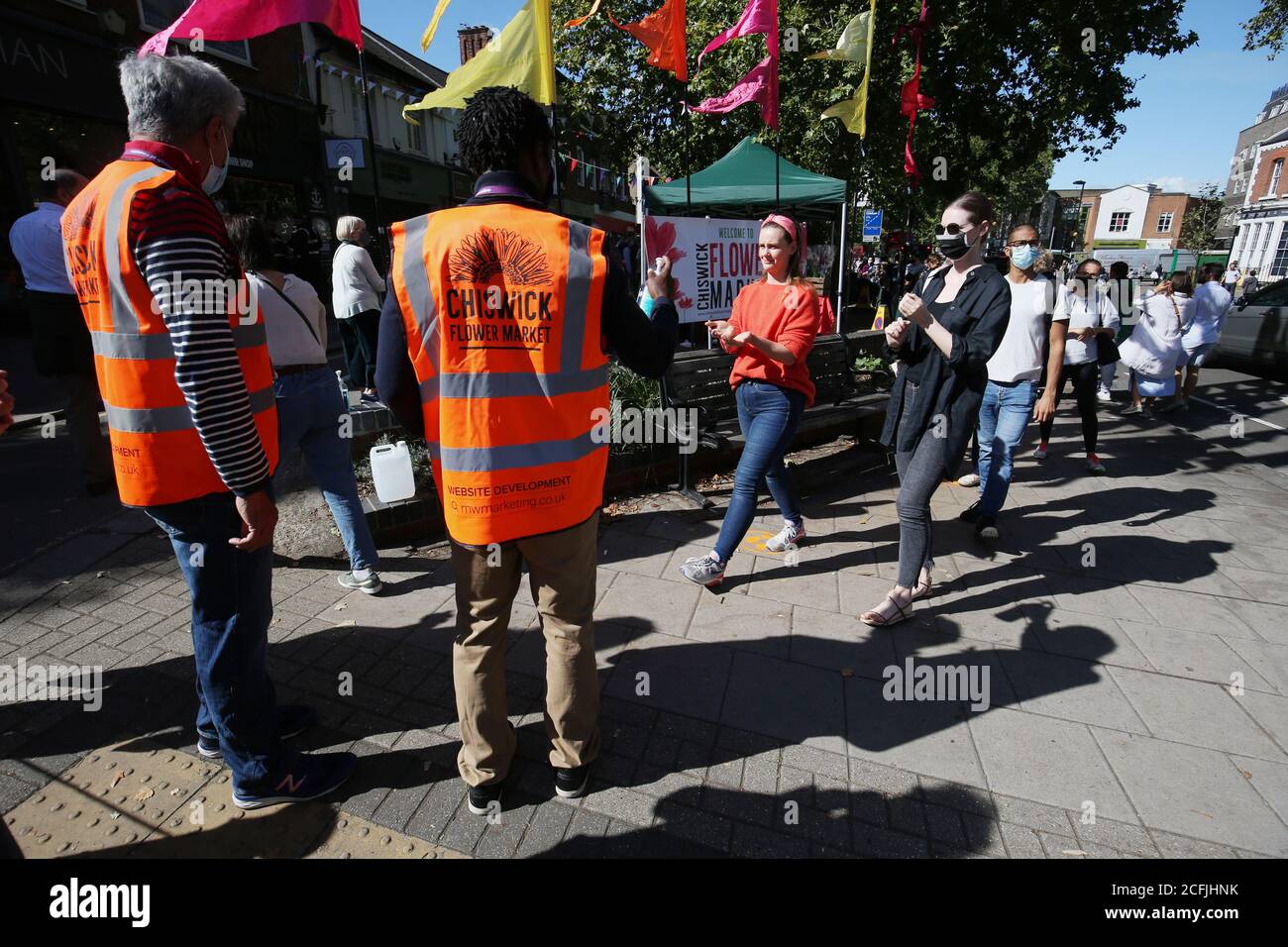 Stewards geben Desinfektionsmittel aus der Hand an diejenigen, die am Chiswick Flower Market in Londons Stadtteil Hounslow Schlange stehen. Der neue Freiluftmarkt wurde von den Bewohnern gegründet, in der Hoffnung, dass er die lokale Wirtschaft ankurbeln wird, und ist offenbar der erste neue Blumenmarkt in London seit 150 Jahren. Stockfoto