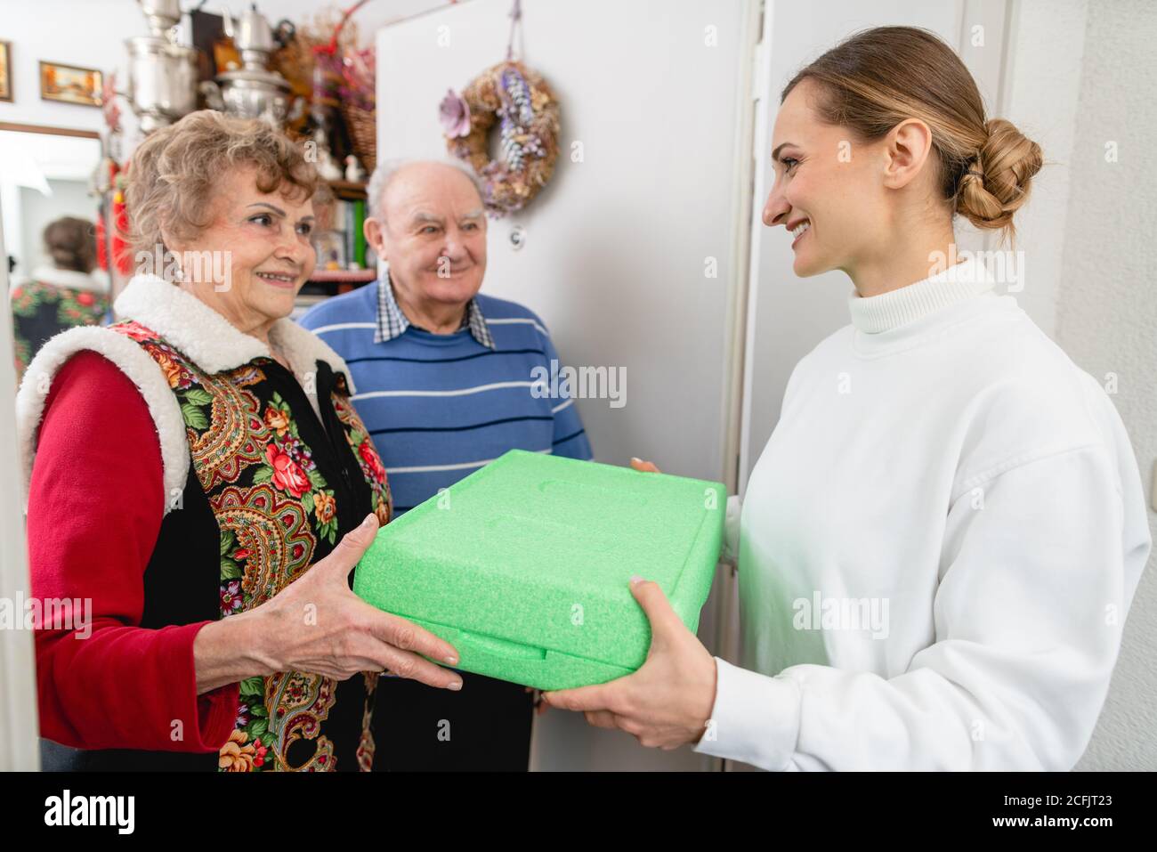 Älteres Paar begrüßt Freiwillige, die eine warme Mahlzeit an ihre Tür liefern Stockfoto