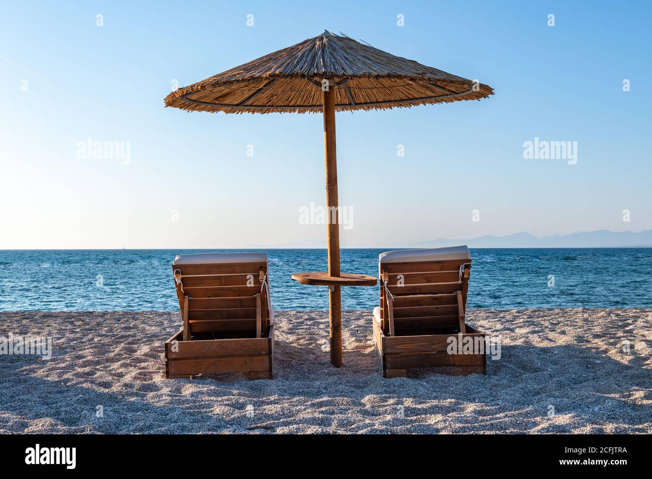 Ein schöner einsamer langer Sandstrand in heißer Sommersonne mit wolkenlosem blauen Himmel und Meer. Stockfoto