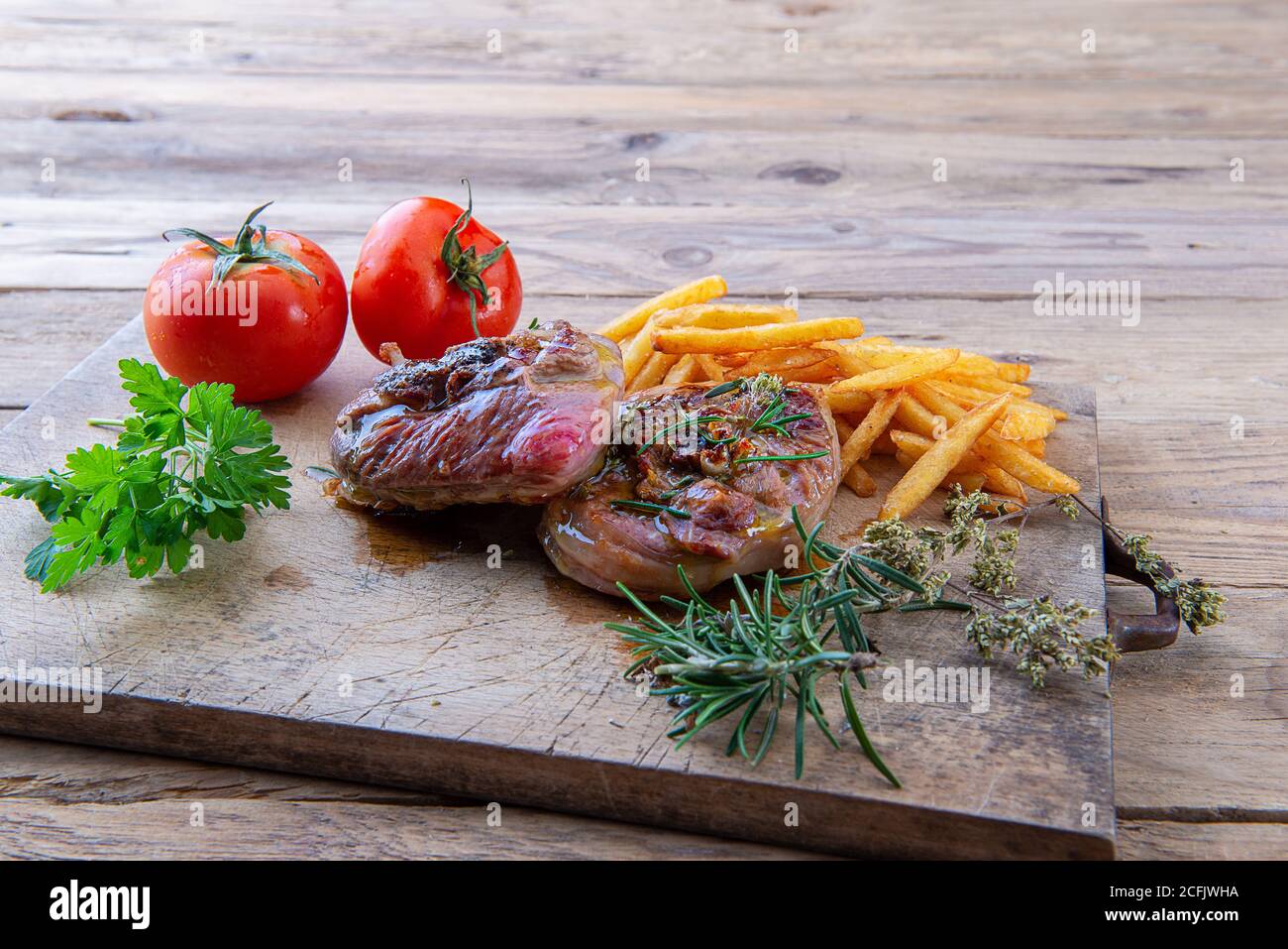 Gegrillter putenossobuco auf einem Schneidebrett mit pommes frites Und Tomaten Stockfoto