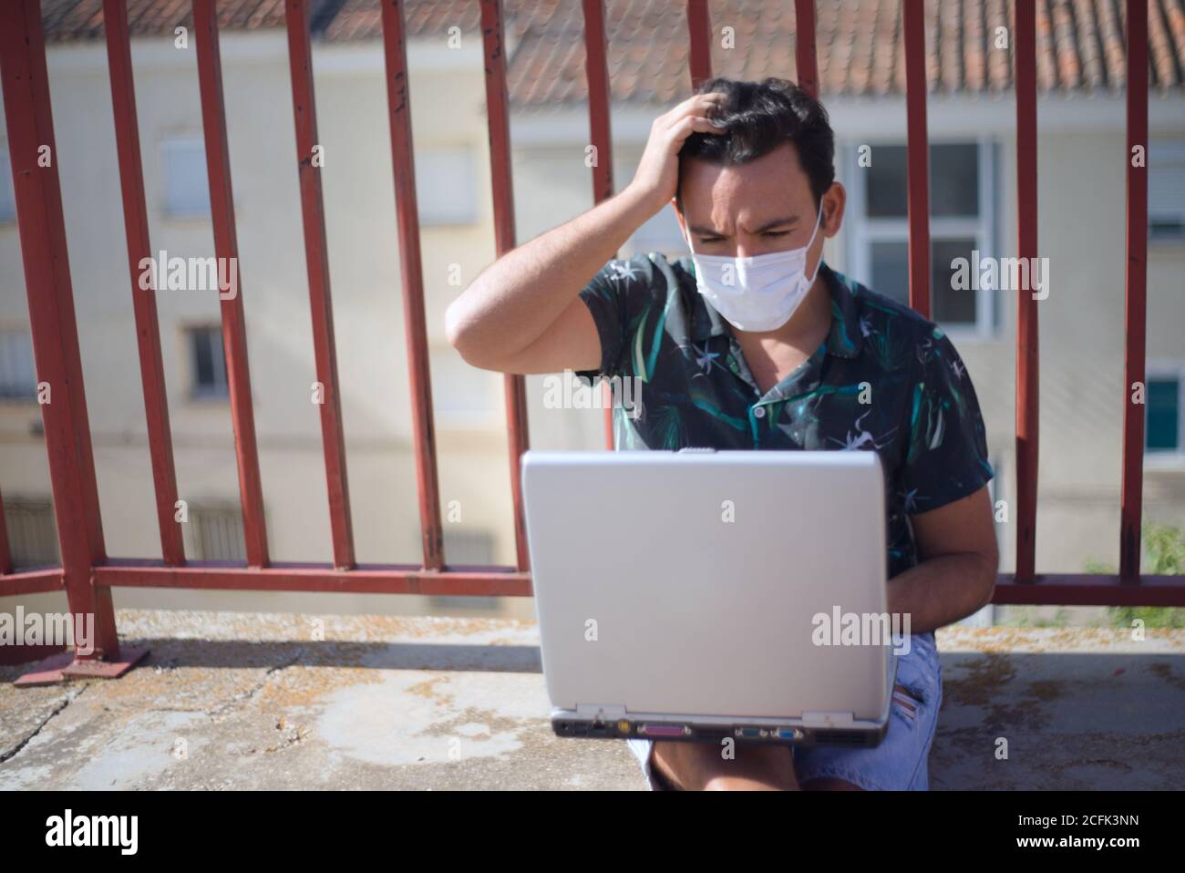 Mann Telearbeit online im Freien mit einem Laptop-Computer und covid Maske. Stockfoto