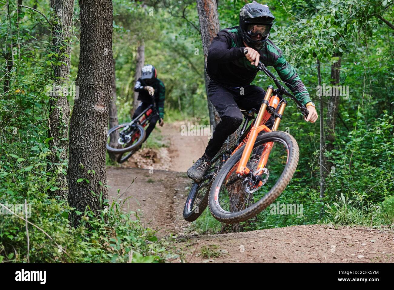 Männliche Radfahrer in Schutzhelmen und Kostümen, die gefährliche Stunts durchführen Auf Rädern für Downhill auf Trail im Wald Stockfoto