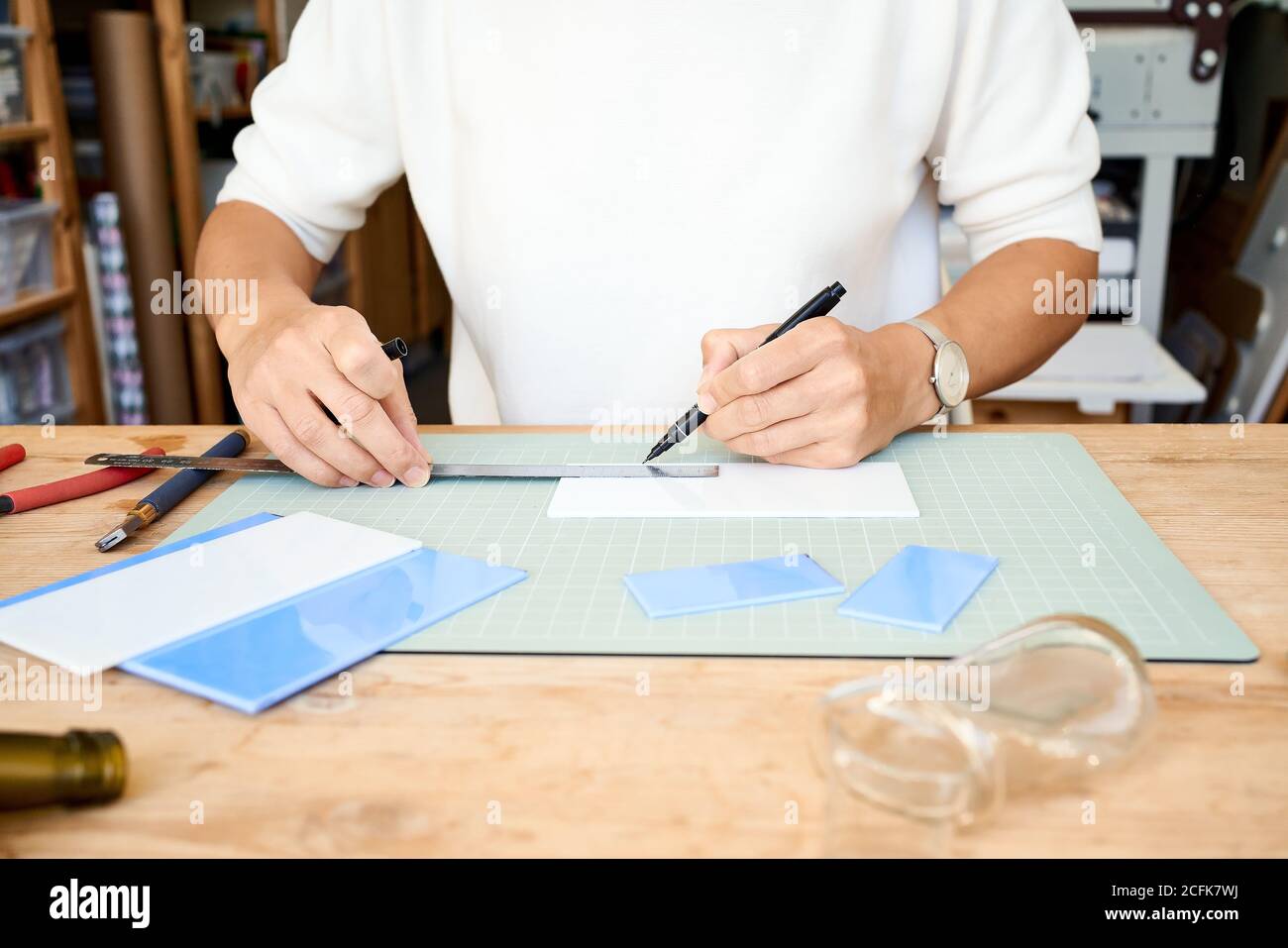 Gesichtslose Unternehmerin, die Glas in einem handwerklichen Arbeitszimmer schneidet. Geschäftsfrau zieht Linie auf Teller, mit Hobby, Seitenrummel Stockfoto