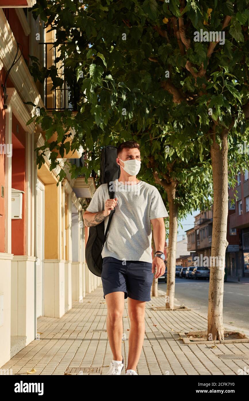 Junger Mann trägt Schutzmaske zu Fuß entlang Bürgersteig auf sonnig Tag bei einem Spaziergang während der Coronavirus-Epidemie Stockfoto