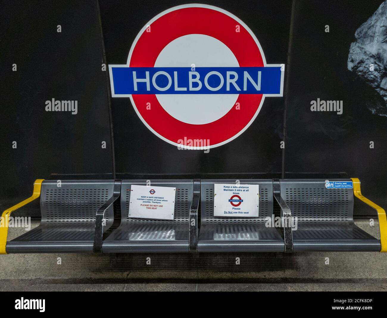 Soziale Distanzierungshinweise an den Sitzplätzen auf dem Bahnsteig der Londoner U-Bahn-Station Holborn. Stockfoto