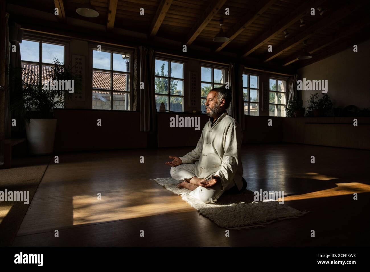 Ganzkörper-Seitenansicht des fokussierten bärtigen ethnischen älteren Mannes Chi-Kung-Meditation in Lotusposition im dunklen Studio üben Stockfoto