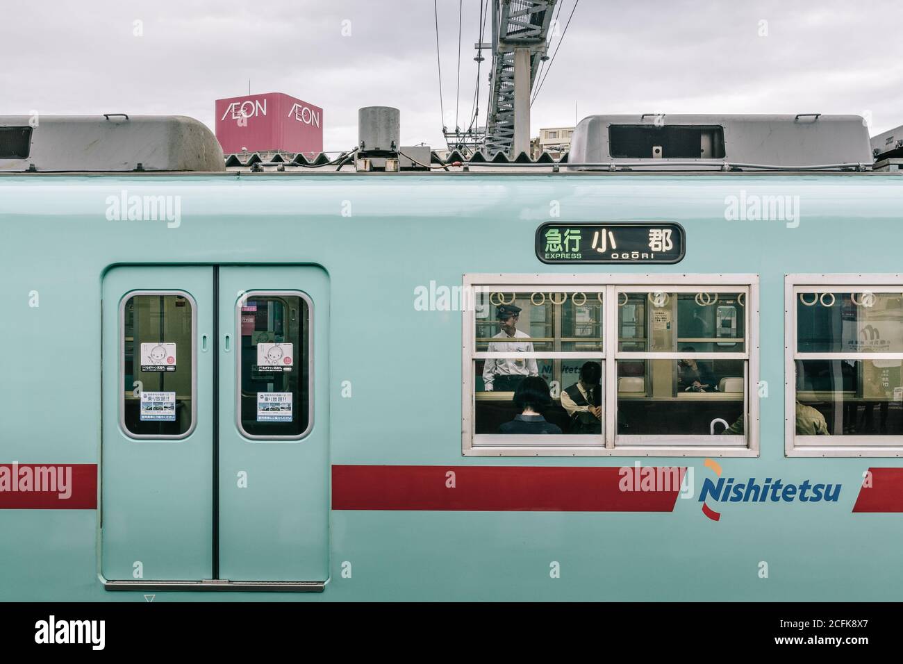 Dazaifu, Fukuoka, Japan - der Schnellzug wartet auf dem Bahnsteig. Sicherheitspersonal, das hinter dem Zug am städtischen Bahnhof steht. Stockfoto