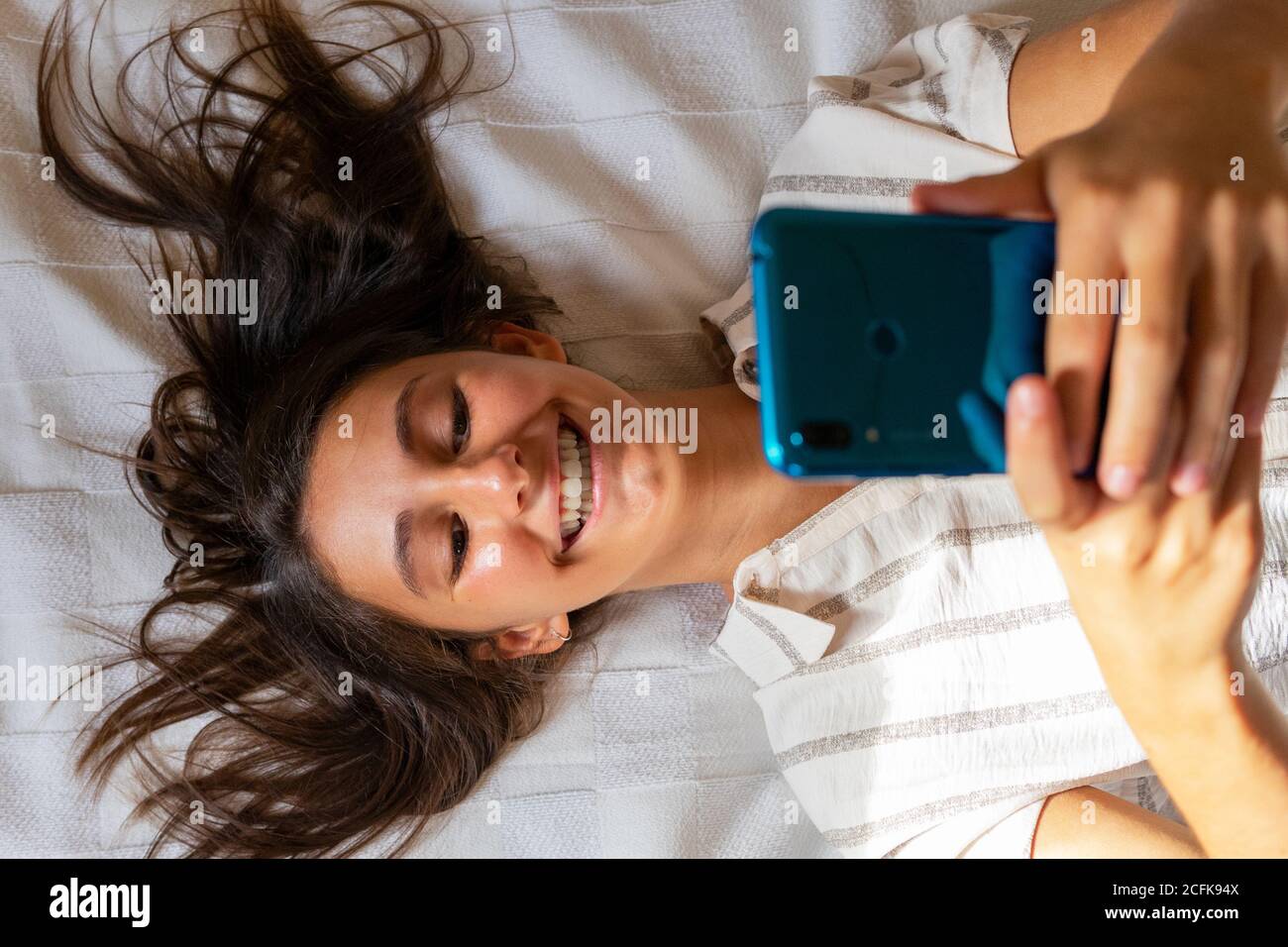 Von oben erfreut Weibchen liegend auf dem weichen Bett bei Home und Lesen von Nachrichten in sozialen Medien über das Mobiltelefon Stockfoto