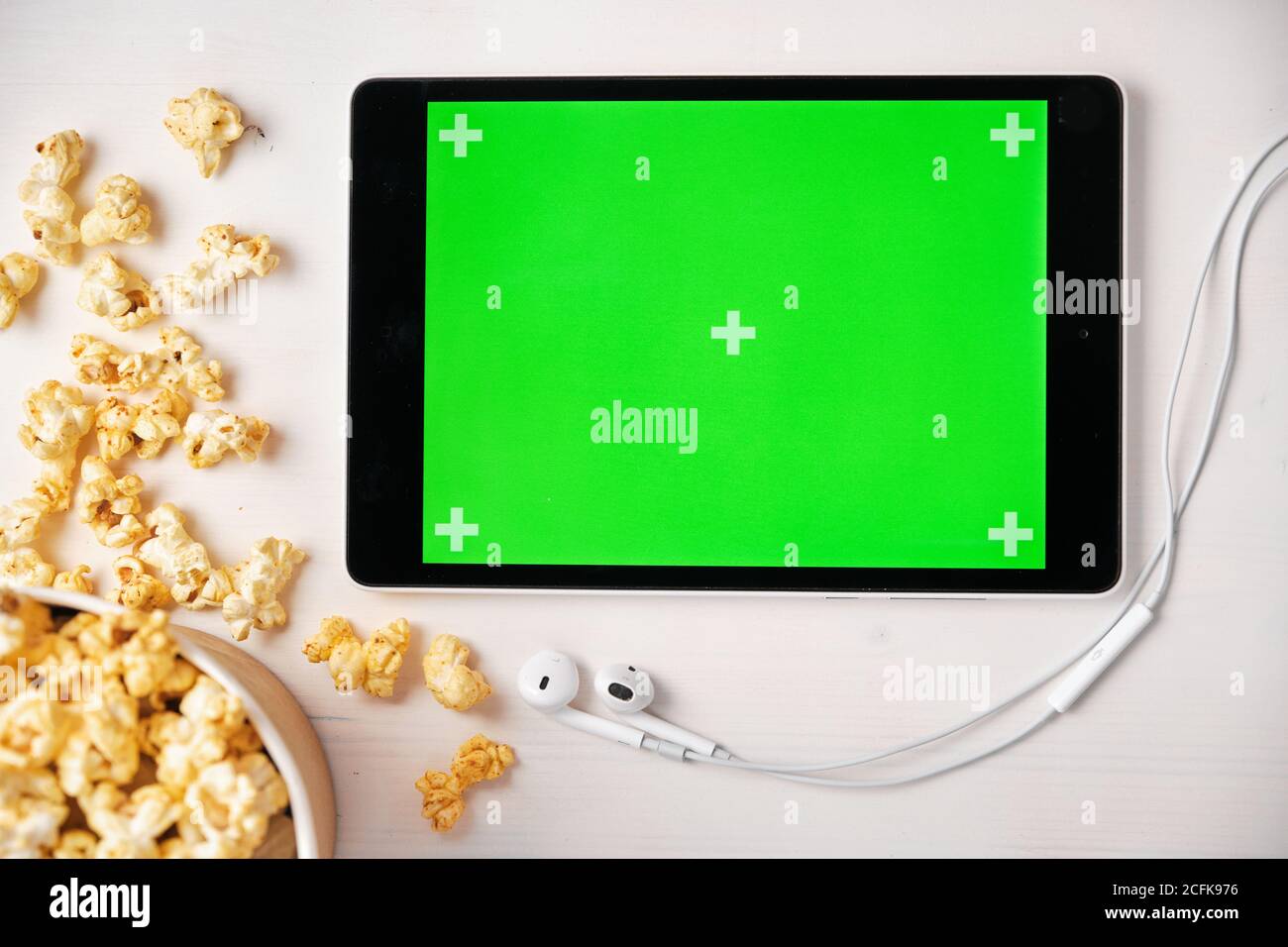 Tablet mit Chroma-Key, Popcorn-Box und Apple-Kopfhörer auf dem weißen Tisch. Platz für Werbung und Logo. Stockfoto