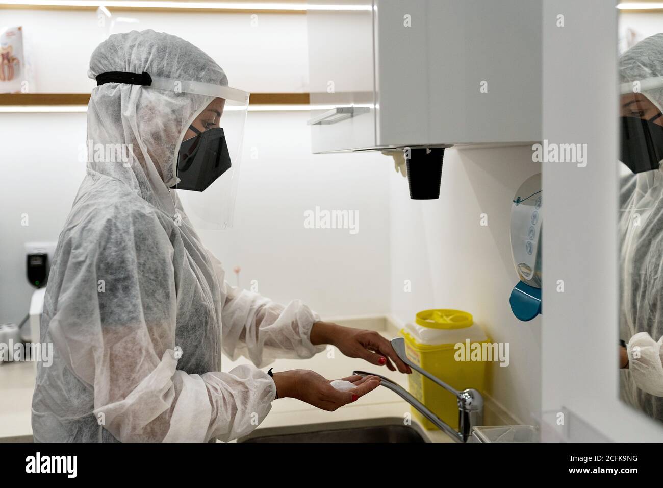 Seitenansicht der Ärztin in Schutzanzug und Gesicht Schild mit Maske waschen Hände während der Vorbereitung für den medizinischen Eingriff In der modernen Klinik Stockfoto