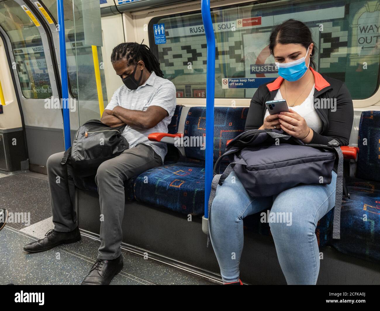 Passagiere im Londoner U-Bahn-Wagen tragen Gesichtsbezüge und versuchen, soziale Distanzierung zu üben. Stockfoto