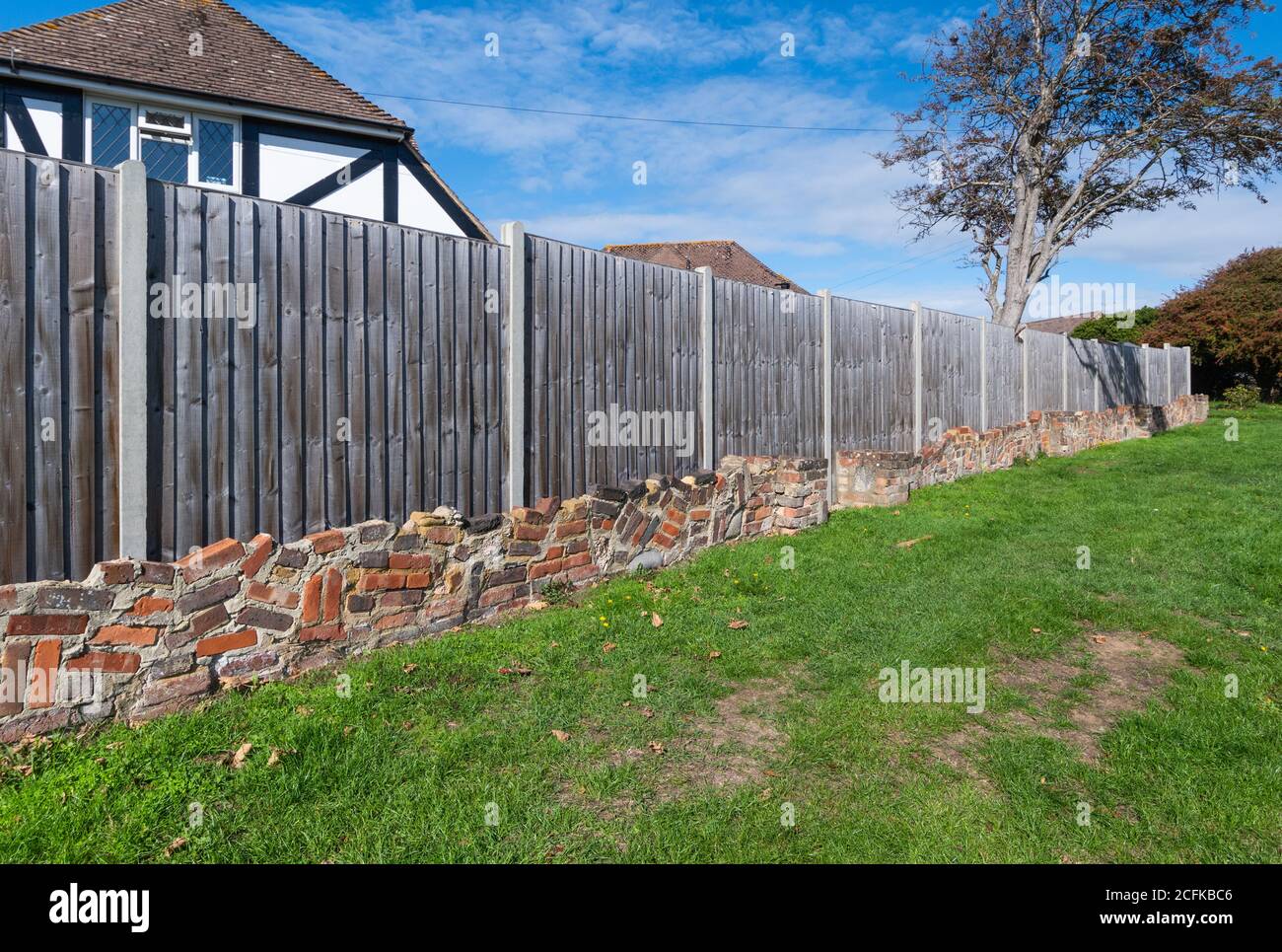 Dekorative niedrige Ziegelwand mit Holzeinzäunung im Closeboard-Stil mit vertikalen Federleisten am Ende eines privaten Gartens in England, Großbritannien. Stockfoto