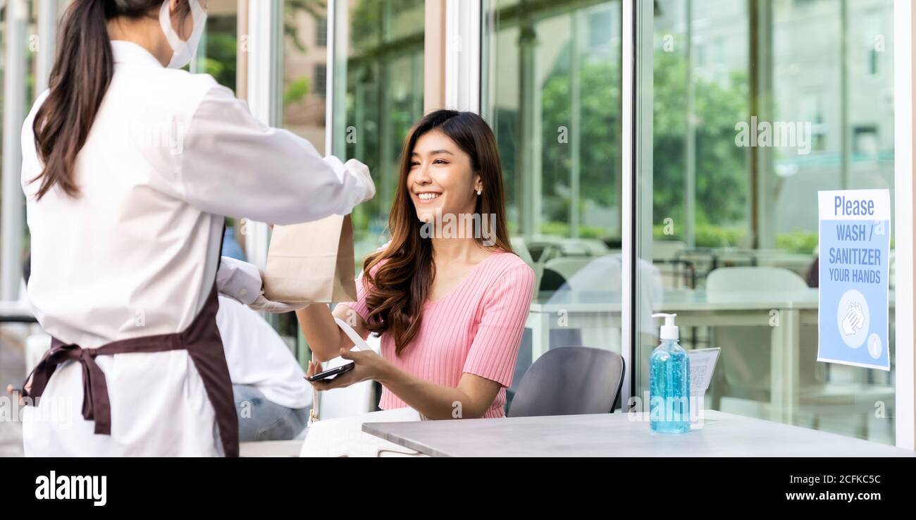 Panoramablick auf attraktive Frau weiblichen Kunden nehmen aus Lebensmittelbeutel bestellen von Kellnerin tragen Gesichtsmaske. Essen zum Mitnehmen oder zum Mitnehmen Stockfoto