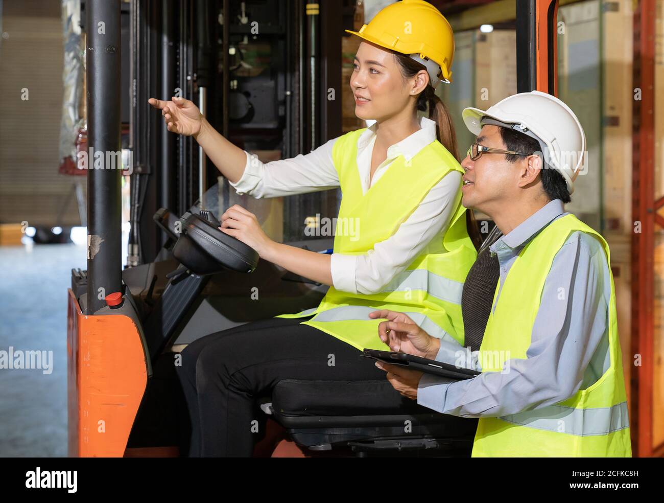 Weibliche junge asiatische Lager Gabelstapler Arbeiter diskutieren über Inventar zu männlichen Lagerleiter in großen Ablenkungslager Hintergrund. Erneut Öffnen Stockfoto