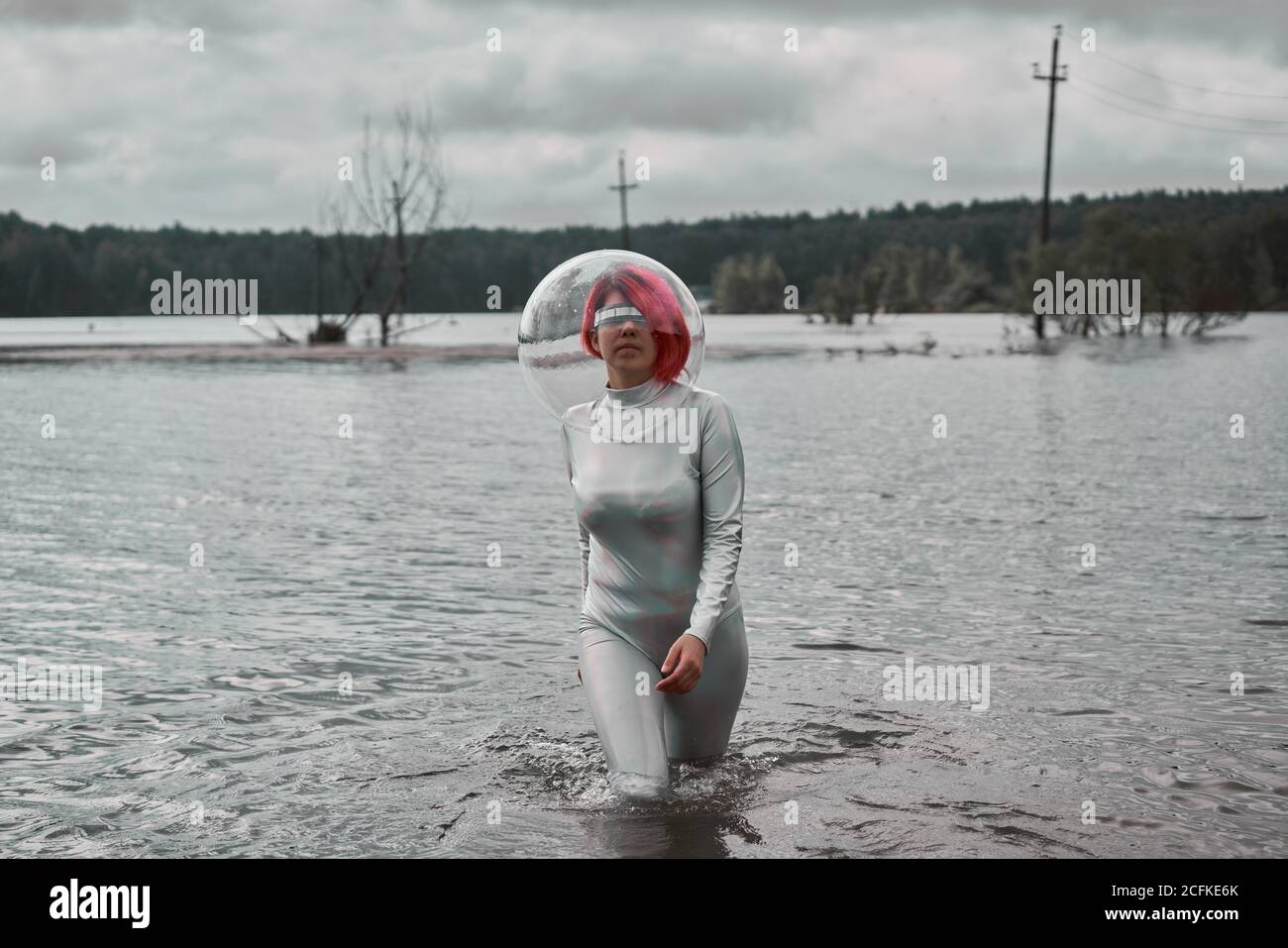 Futuristische junge rothaarige Frau in silbernen Raumanzug und Glashelm, der aus dem Fluten des Flusses herausläuft Stockfoto