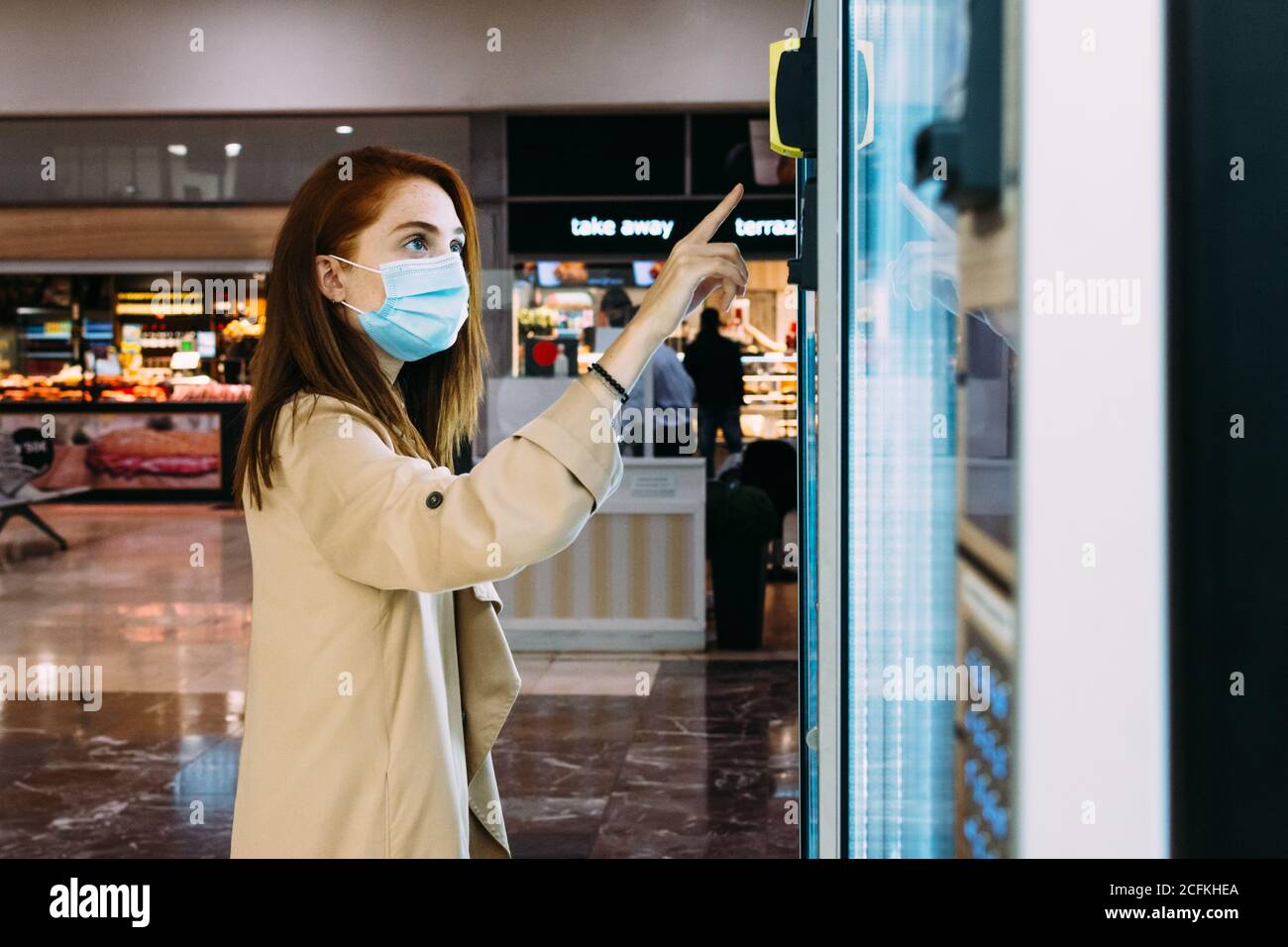 Frau mit einer Gesichtsmaske nutzt den Automaten zu Kaufen Sie einen Snack Stockfoto