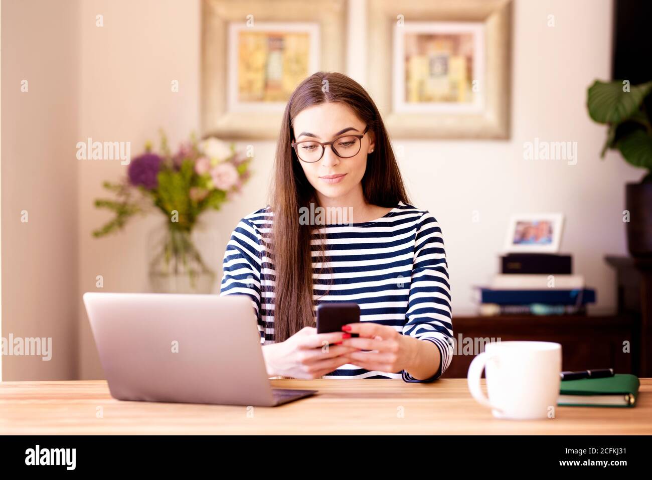 Portait Aufnahme von lächelnden jungen Frau Textnachrichten, während sie am Schreibtisch sitzt und von zu Hause aus arbeitet. Home Office. Stockfoto