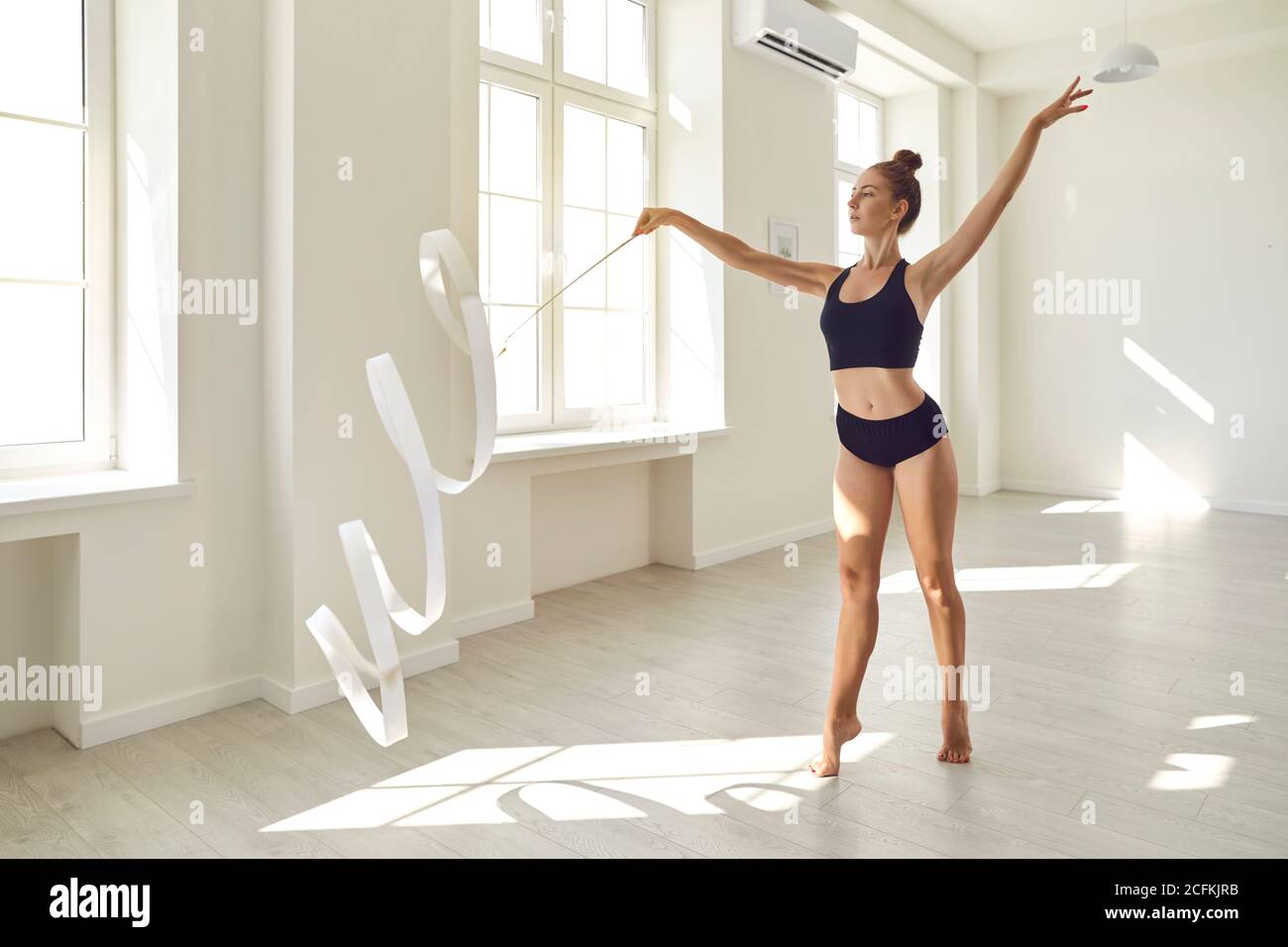 Schöne junge Turnerin mit weißem Band Proben Routine bewegt sich in Modernes Tanzstudio Stockfoto