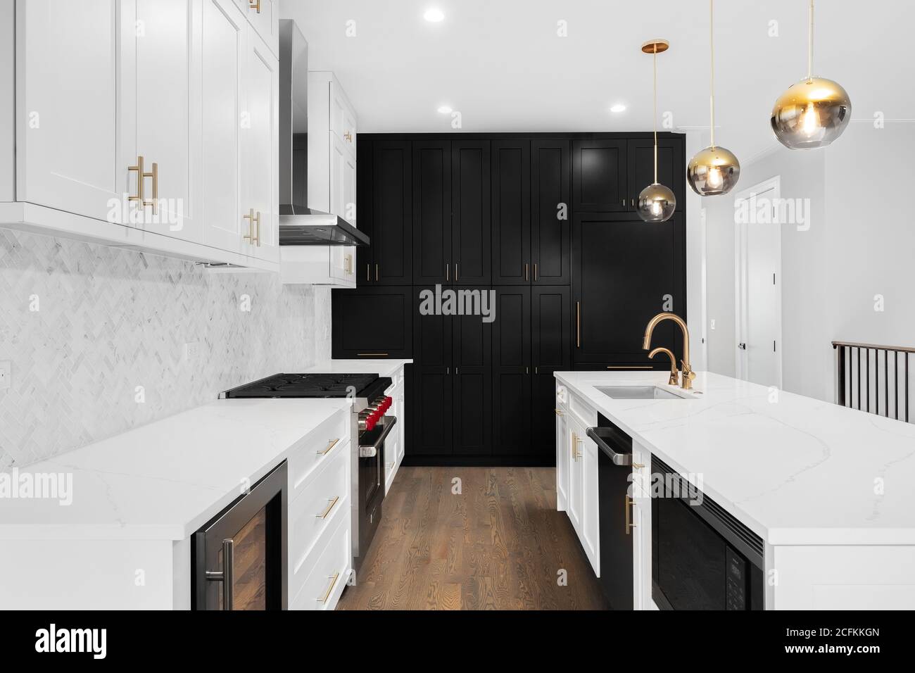 Eine luxuriöse, moderne Küche mit weißen und schwarzen Schränken, goldenen Armaturen und weißen Fischgrätfliesen. Stockfoto