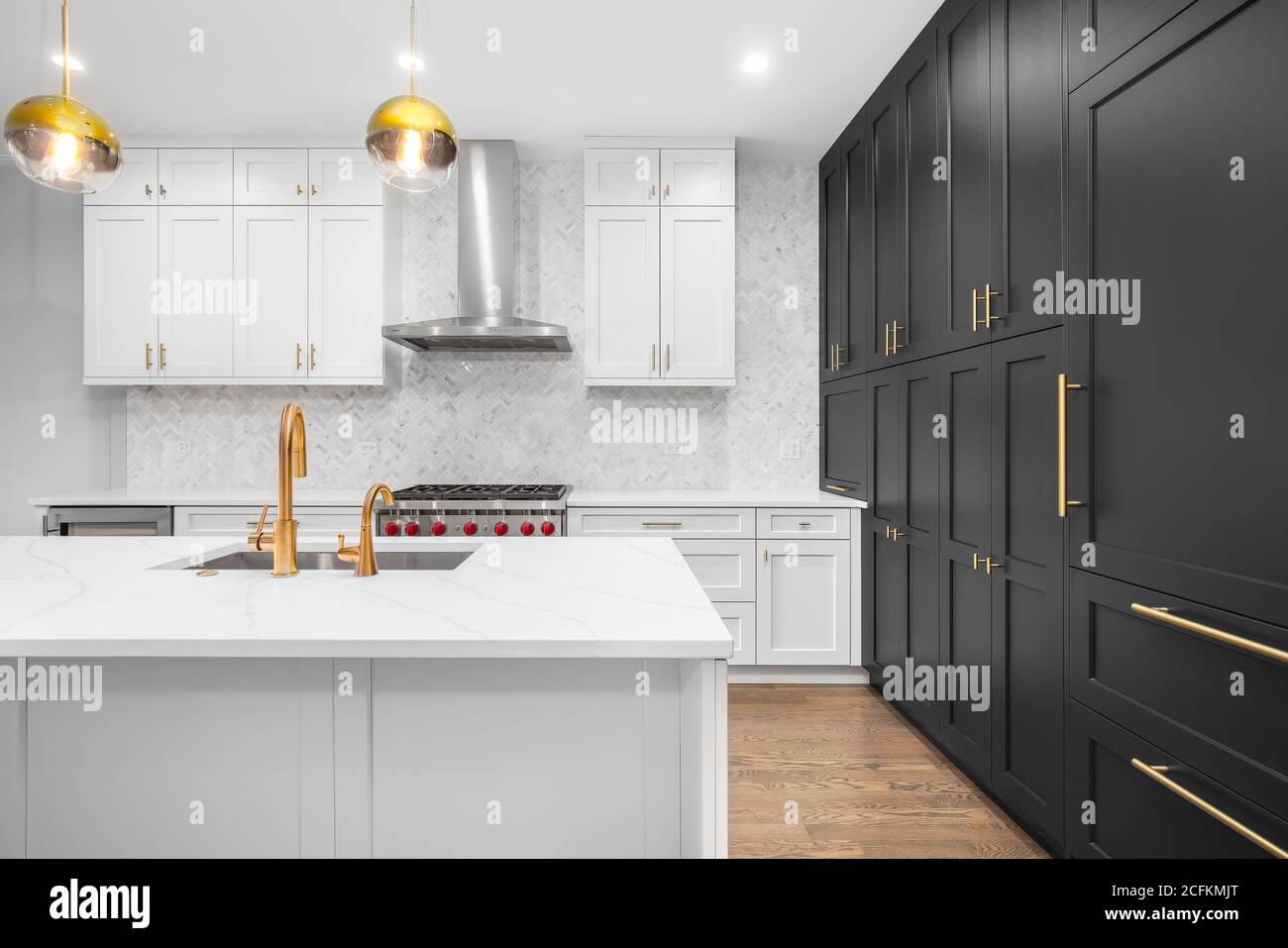 Eine luxuriöse, moderne Küche mit weißen und schwarzen Schränken, goldenen Armaturen und weißen Fischgrätfliesen. Stockfoto