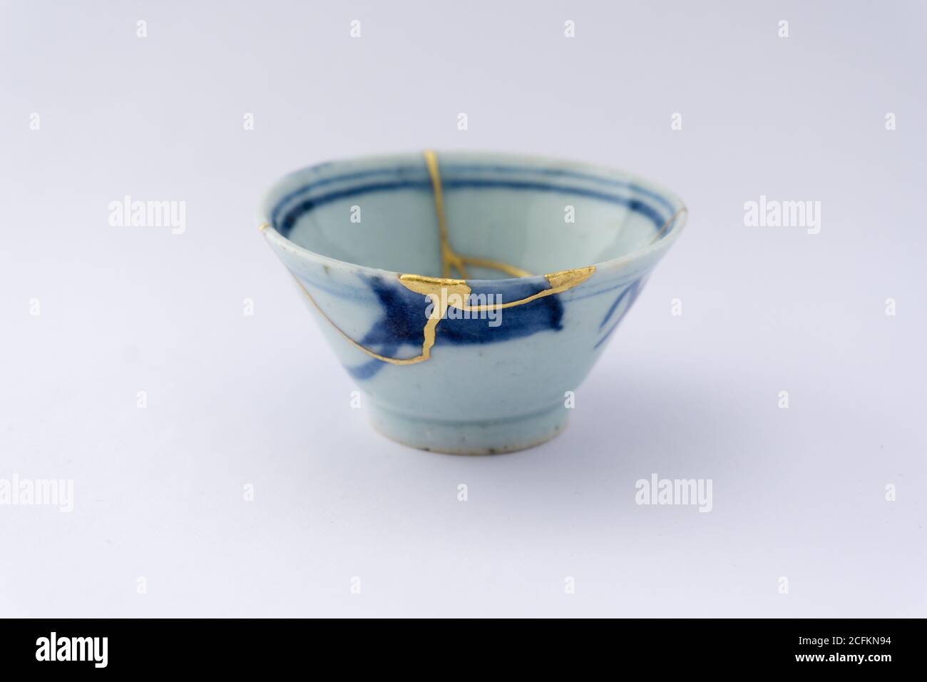 Kintsugi beige weiß und blau, Sake Tasse. Gold Risse Restaurierung auf alten japanischen Keramik. Stockfoto