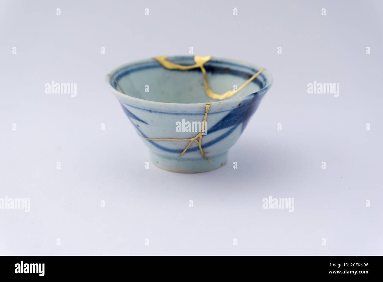 Kintsugi beige weiß und blau, Sake Tasse. Gold Risse Restaurierung auf alten japanischen Keramik. Stockfoto
